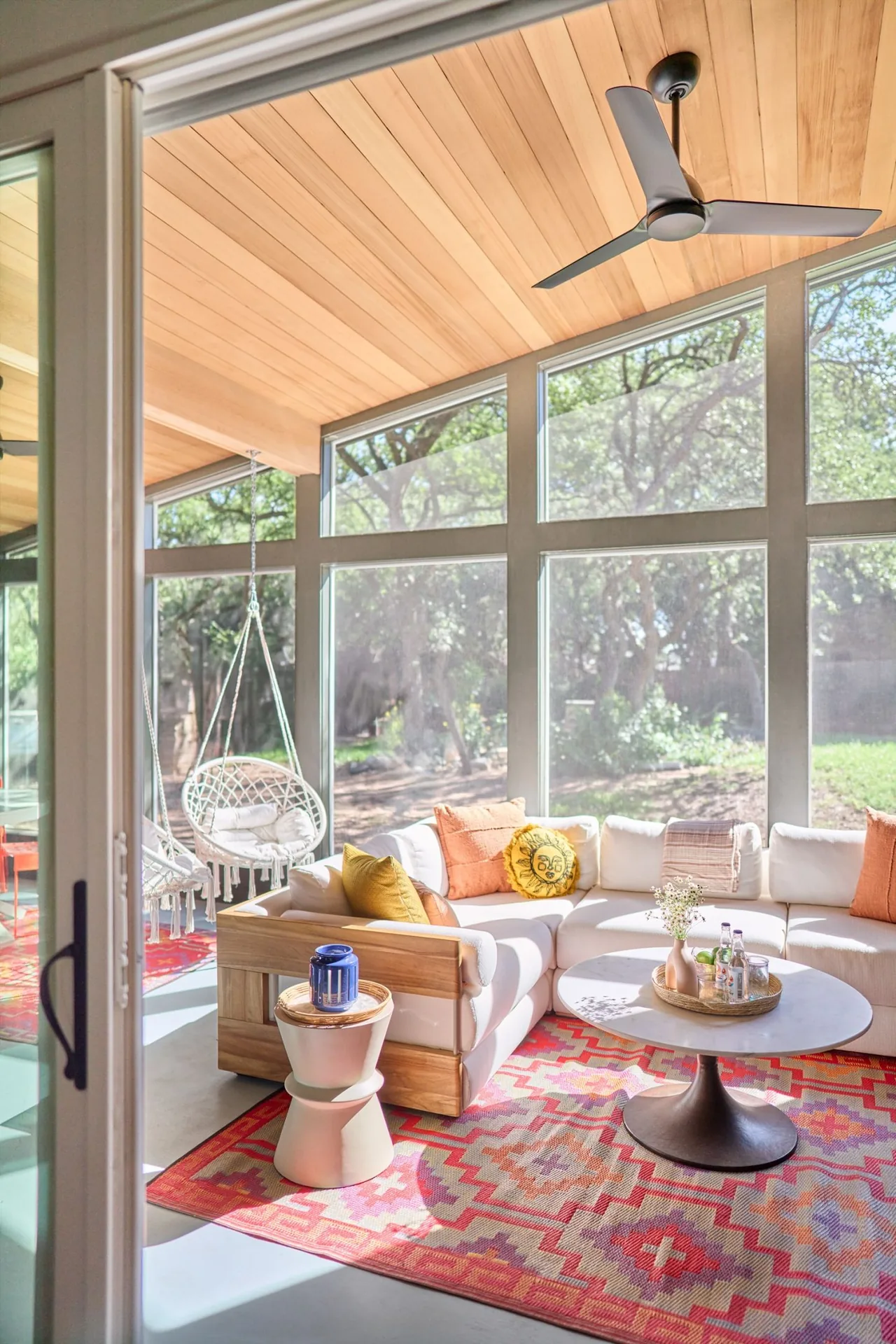Sunroom with floor-to-ceiling glazing and wood ceiling, featuring a sectional sofa and vibrant decorative pillows