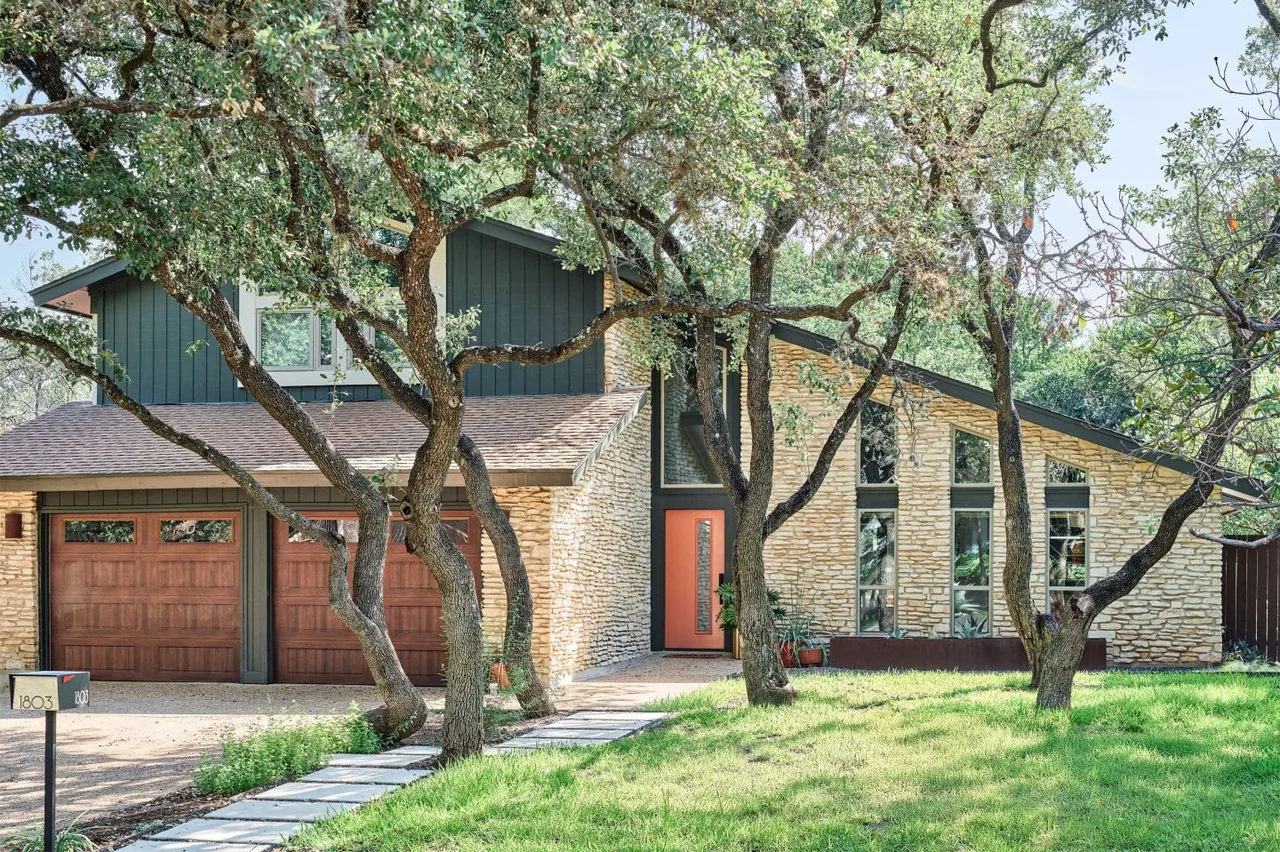 Midcentury modern home with stacked stone walls, a three-car garage, and tall triangular and rectangular windows.