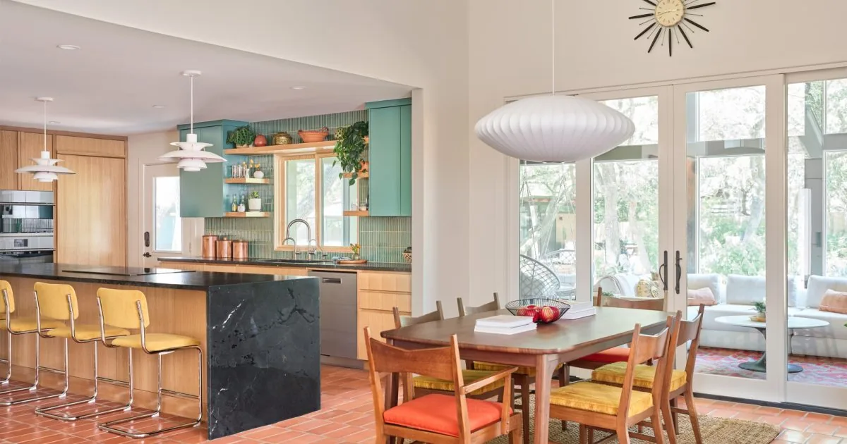 Kitchen with black island countertop and adjacent dining area with mid-century style chairs overlooks outdoor living space.