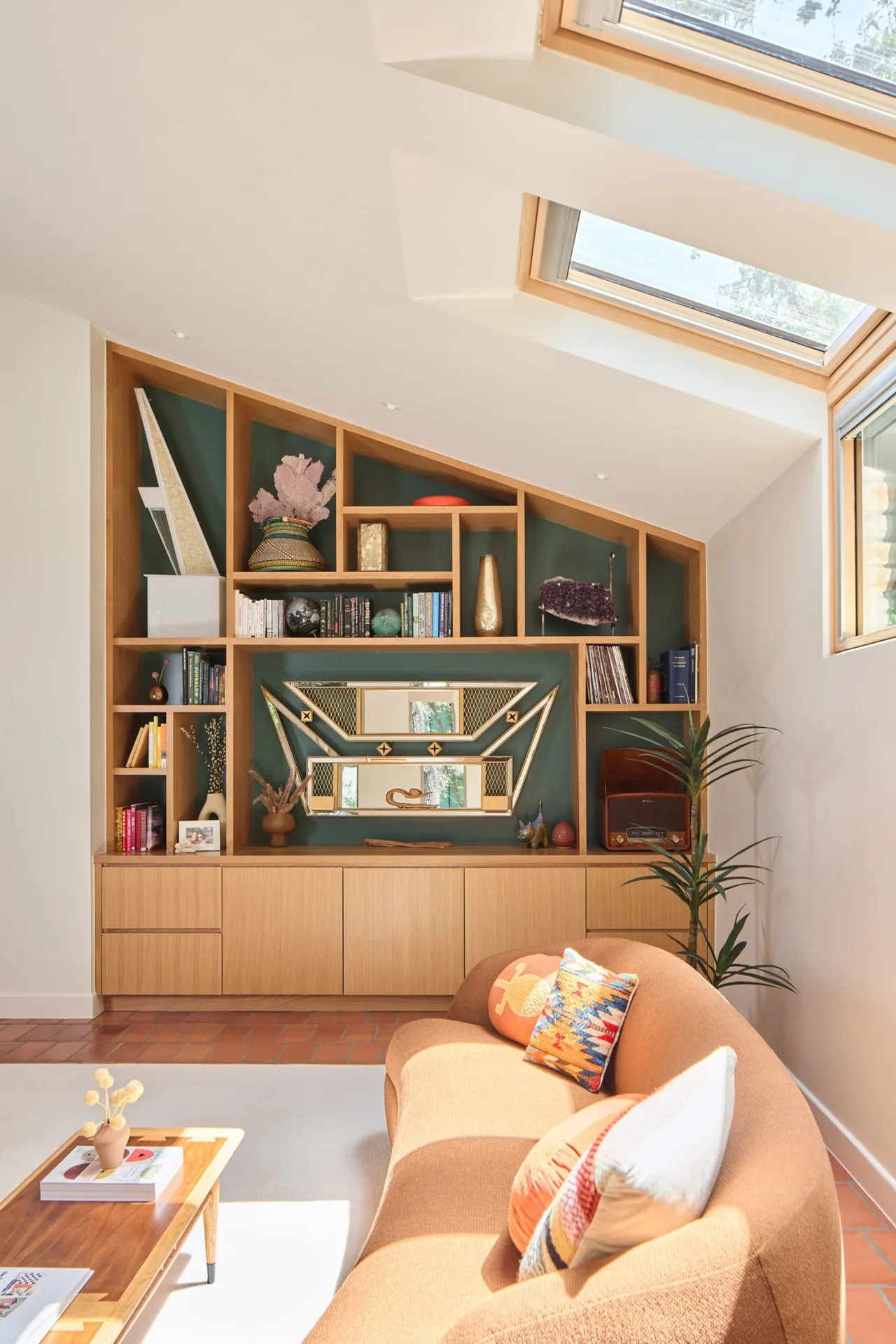 Living room features a curved sofa with bright pillows, custom angled wood shelving, and skylights illuminating the space.