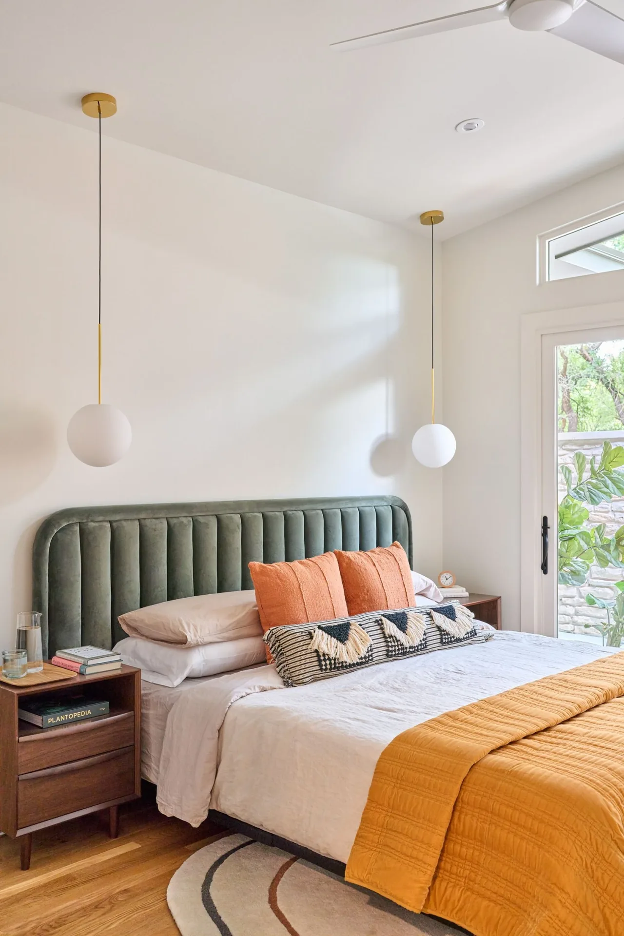 Bedroom featuring a green velvet bed, orange bedding accents, pendant lighting, and access to an outdoor area.