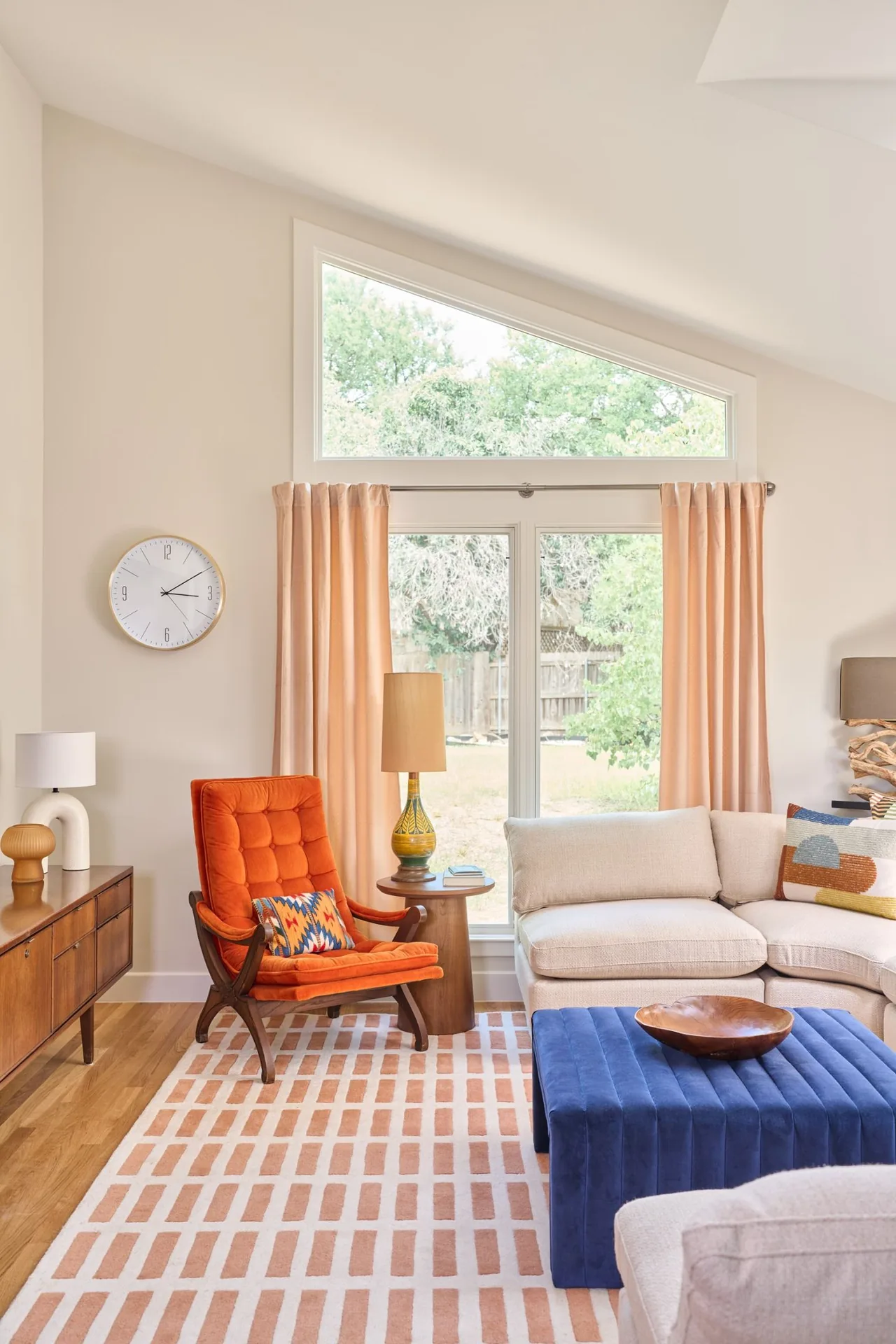 Living room features a beige sectional sofa, orange accent chair, and a blue ottoman beneath a large triangular window.