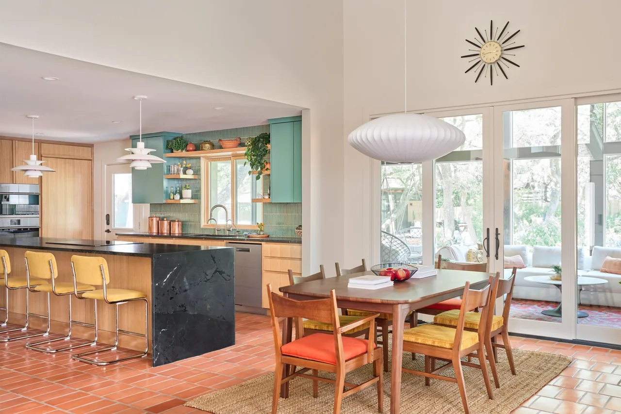 Modern kitchen and dining space with colorful chairs and large glass doors to an outdoor living area.