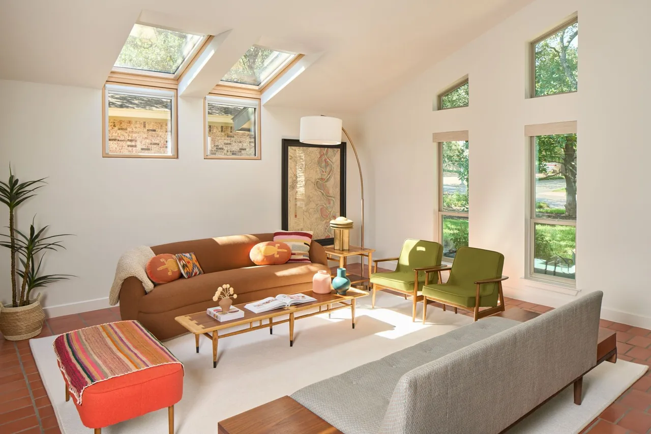 Living room features skylights, triangular clerestory windows, warm terracotta flooring, and modern furnishings with colorful accents.