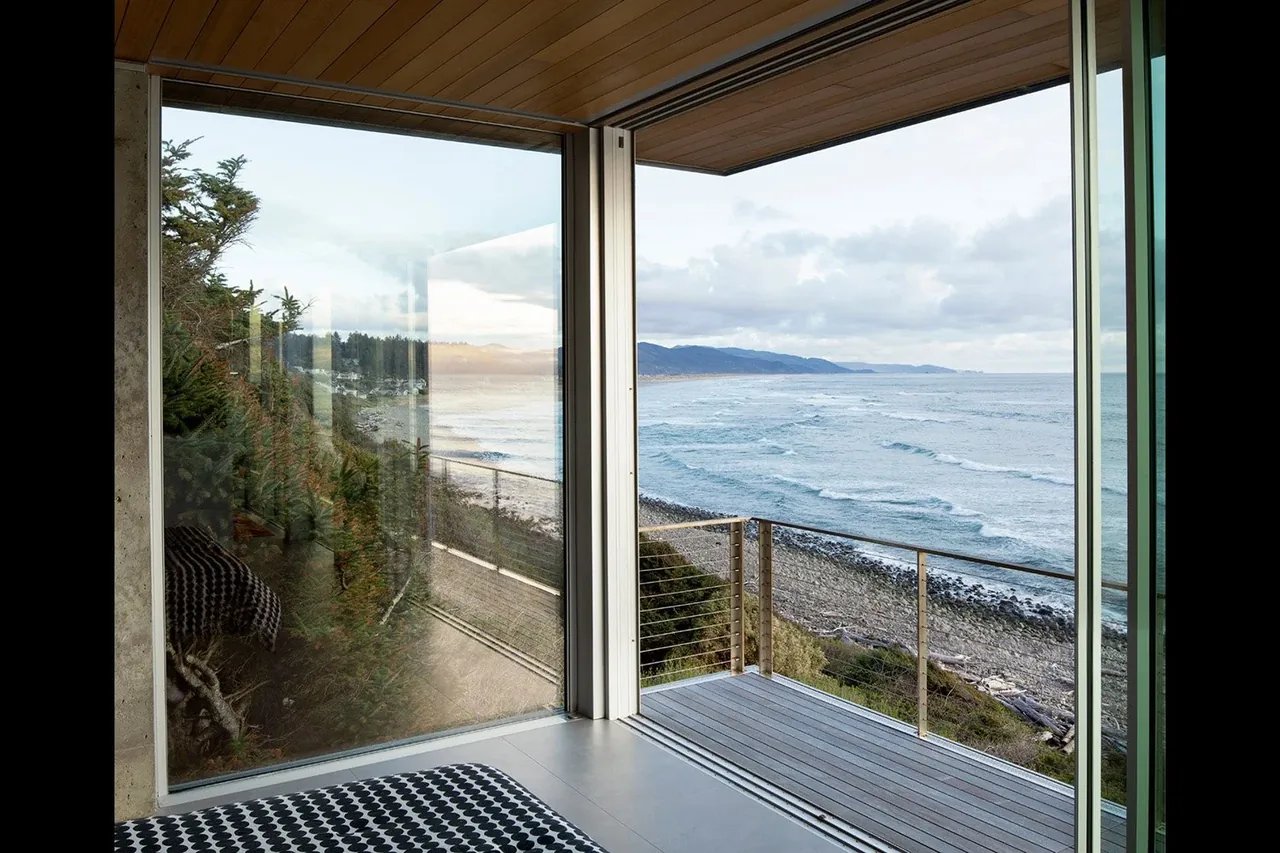 Oceanfront view from a balcony with steel cable railing and wood decking on a contemporary house.