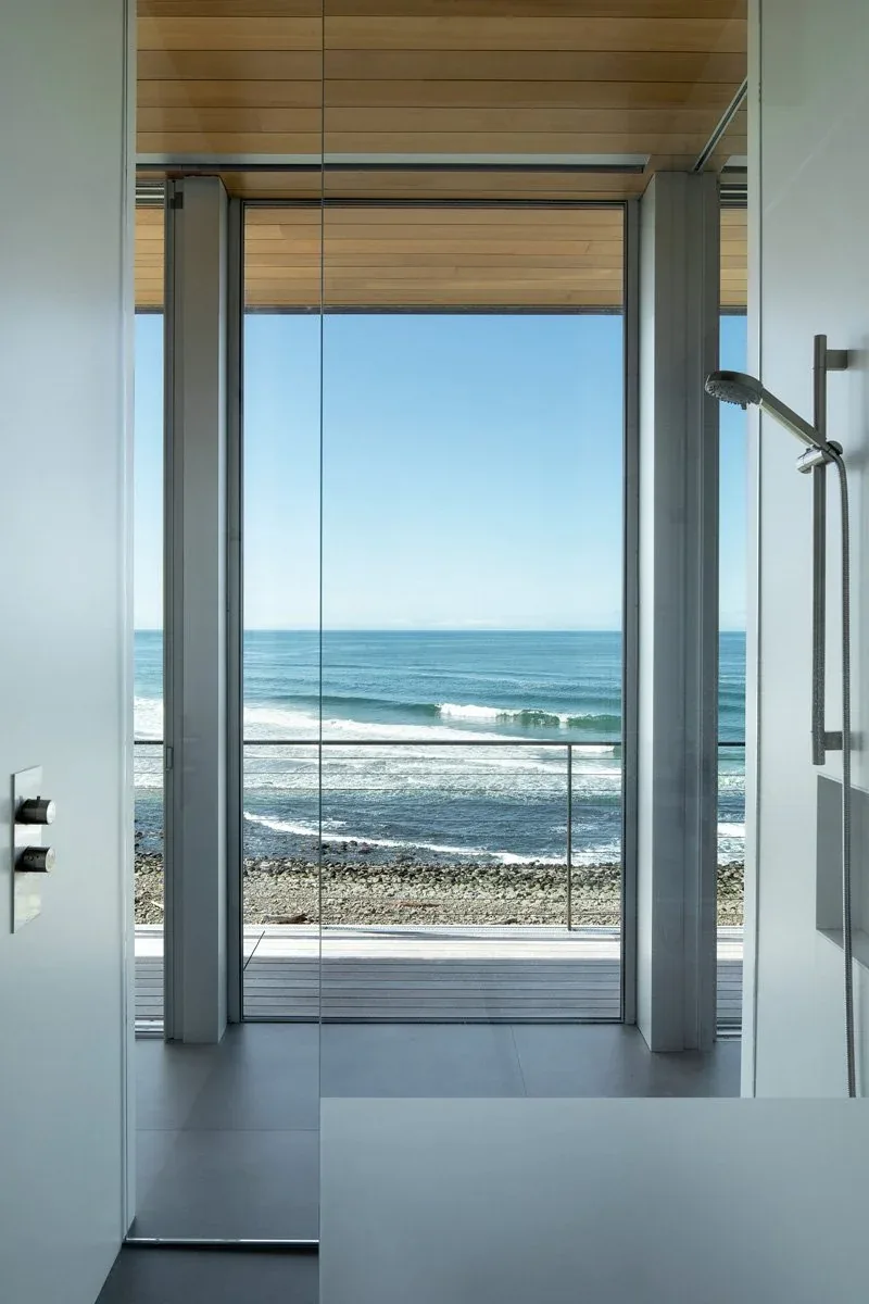 Modern bathroom with floor-to-ceiling glazing overlooking a rocky shoreline and ocean