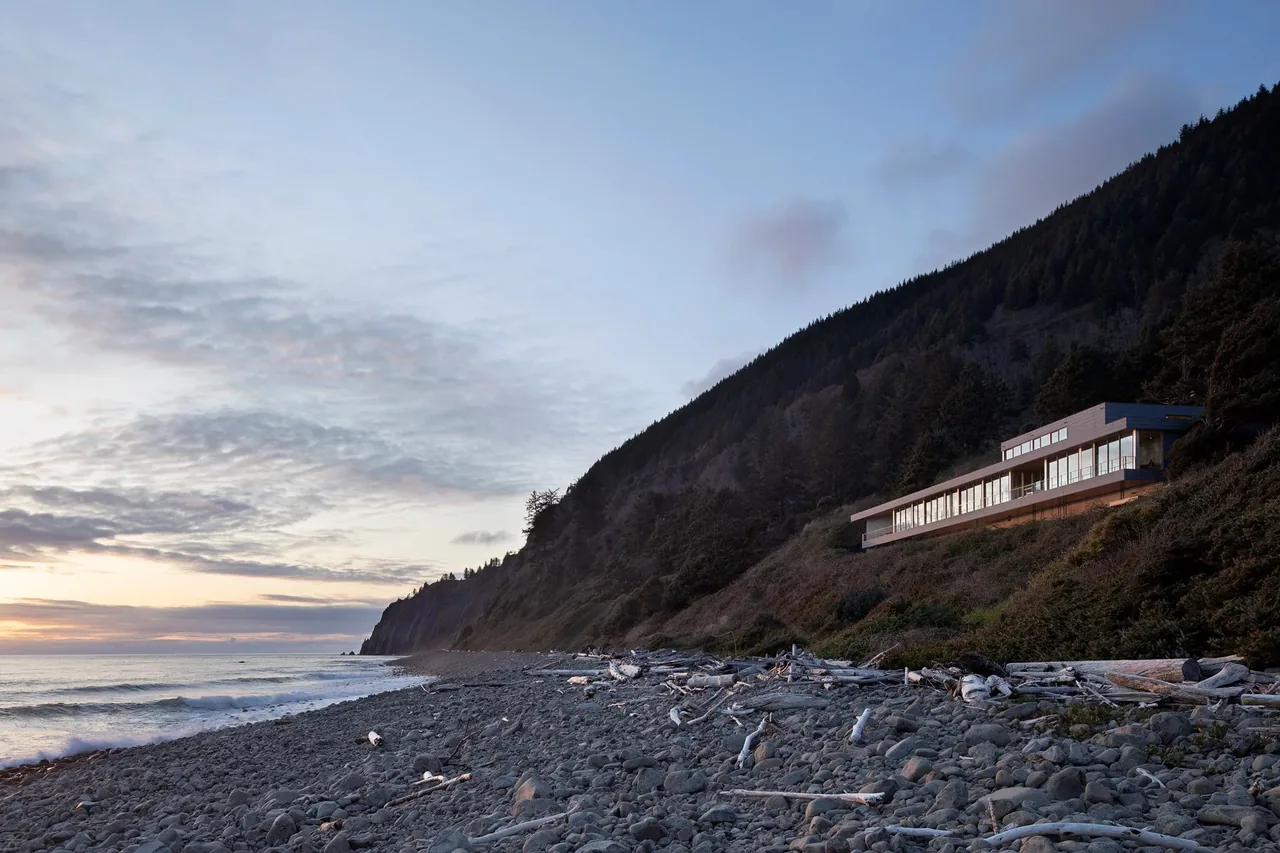 The Prow House by Chadbourne + Doss Architects features expansive glazing on a hillside above a rocky shoreline.