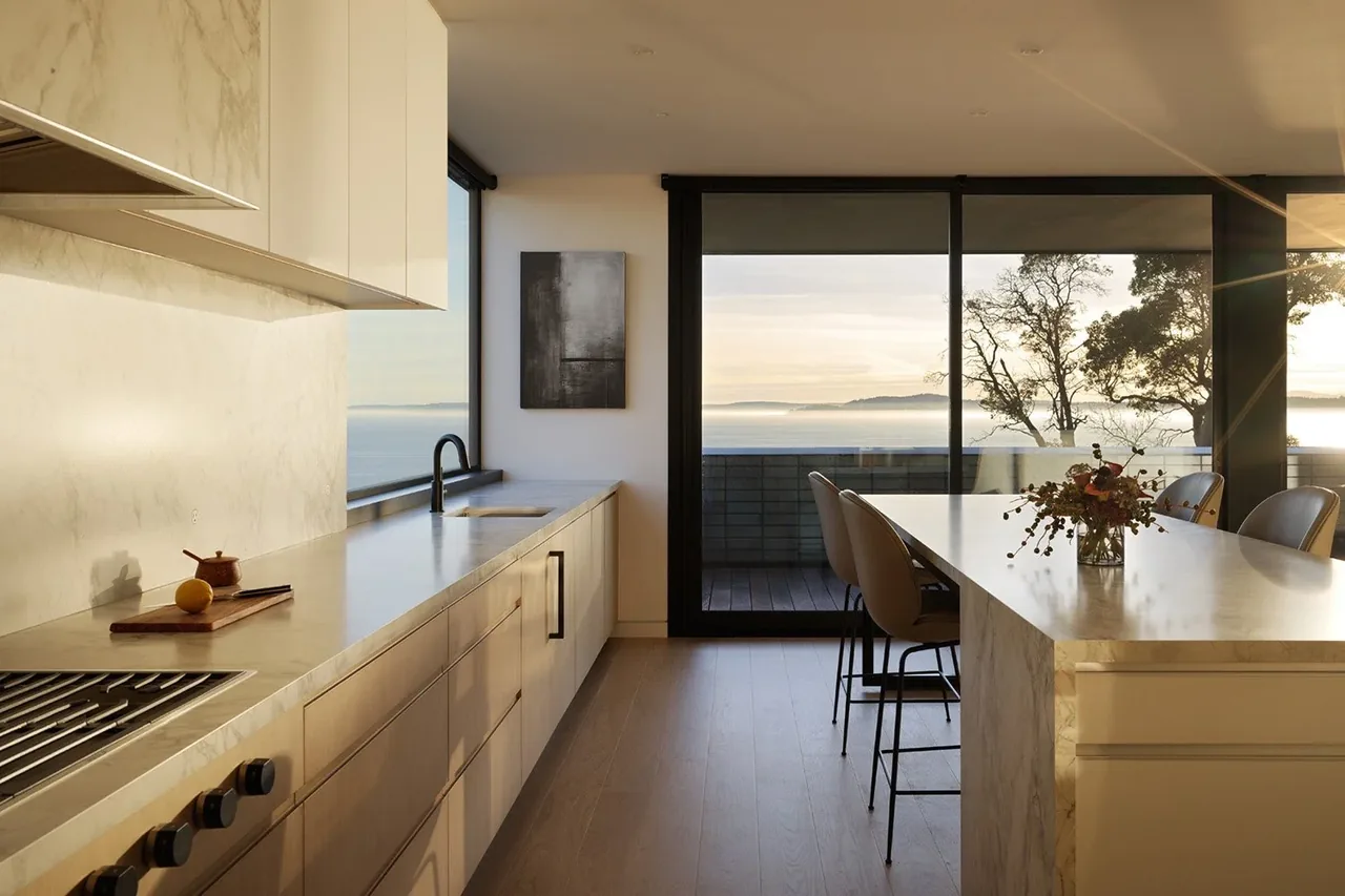 Modern kitchen features marble peninsula, minimal cabinetry, and large glass doors opening to a patio with mountain views.