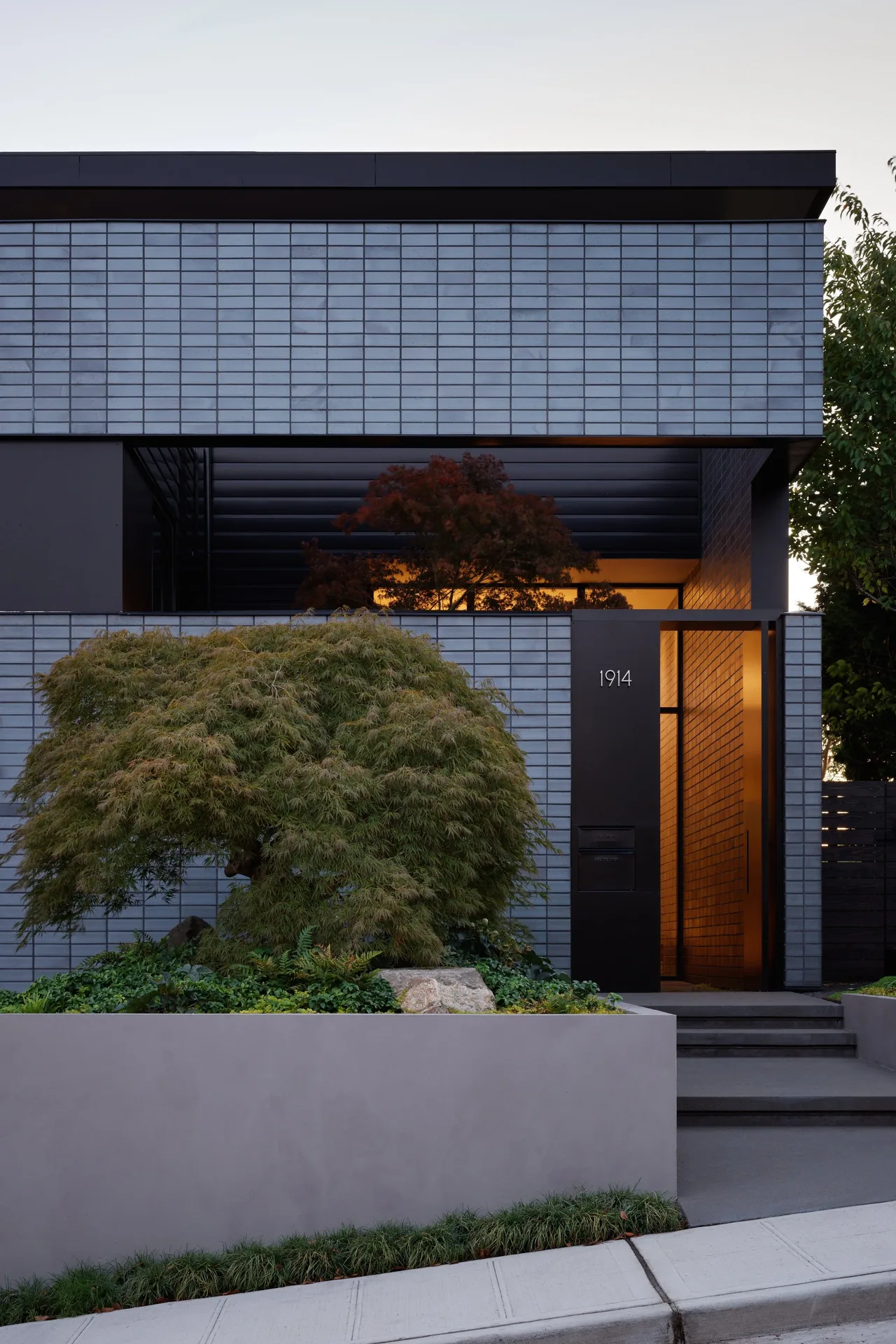 Exterior front of the View Point Residence featuring gray brick cladding and a flat roof, showing the entrance with a black door panel.