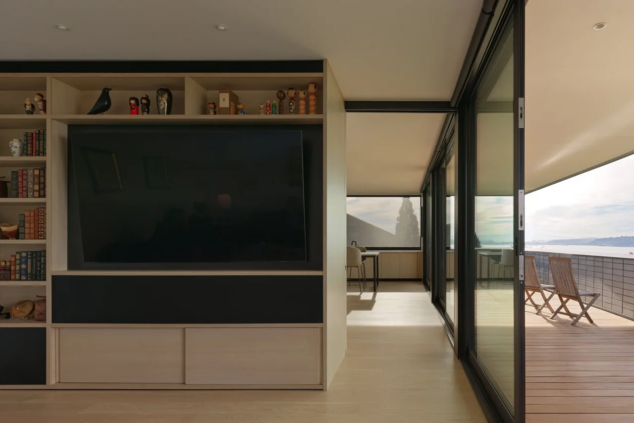 Built-in shelving and TV face a balcony with water views, featuring sliding glass doors and wood flooring.