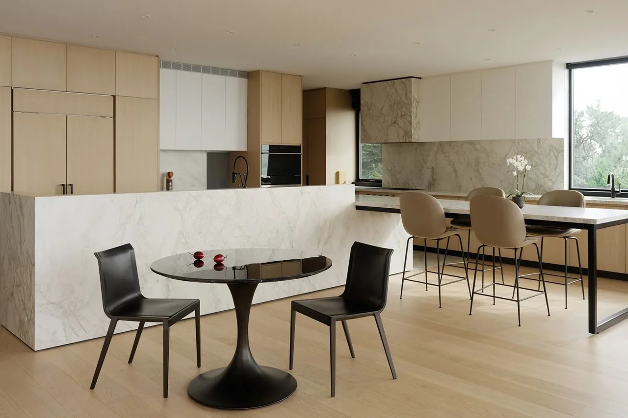 Modern kitchen of the View Point Residence featuring marble countertops and light wood cabinetry paired with a small dining area.