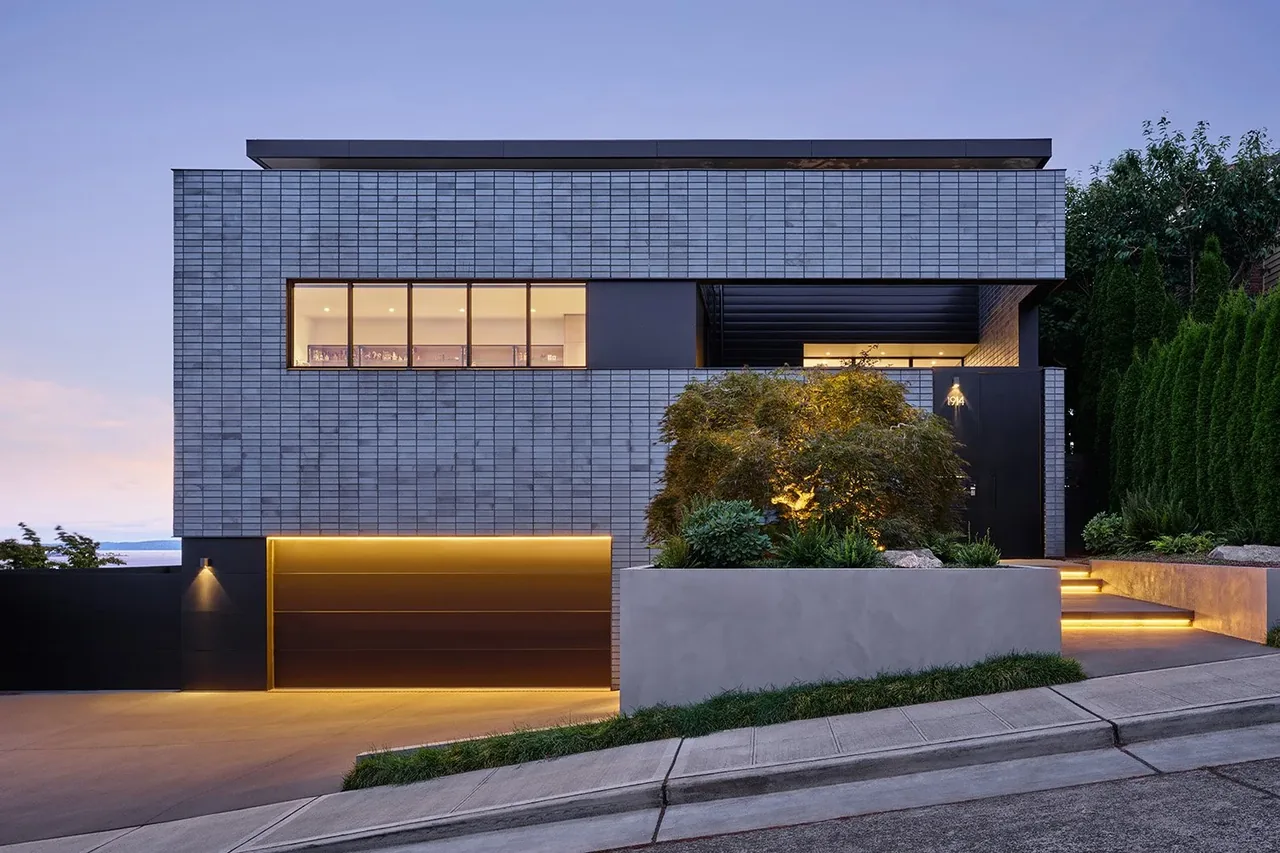 View Point Residence by Chadbourne + Doss Architects features a modern façade with a wood garage door illuminated by warm lighting at dusk.