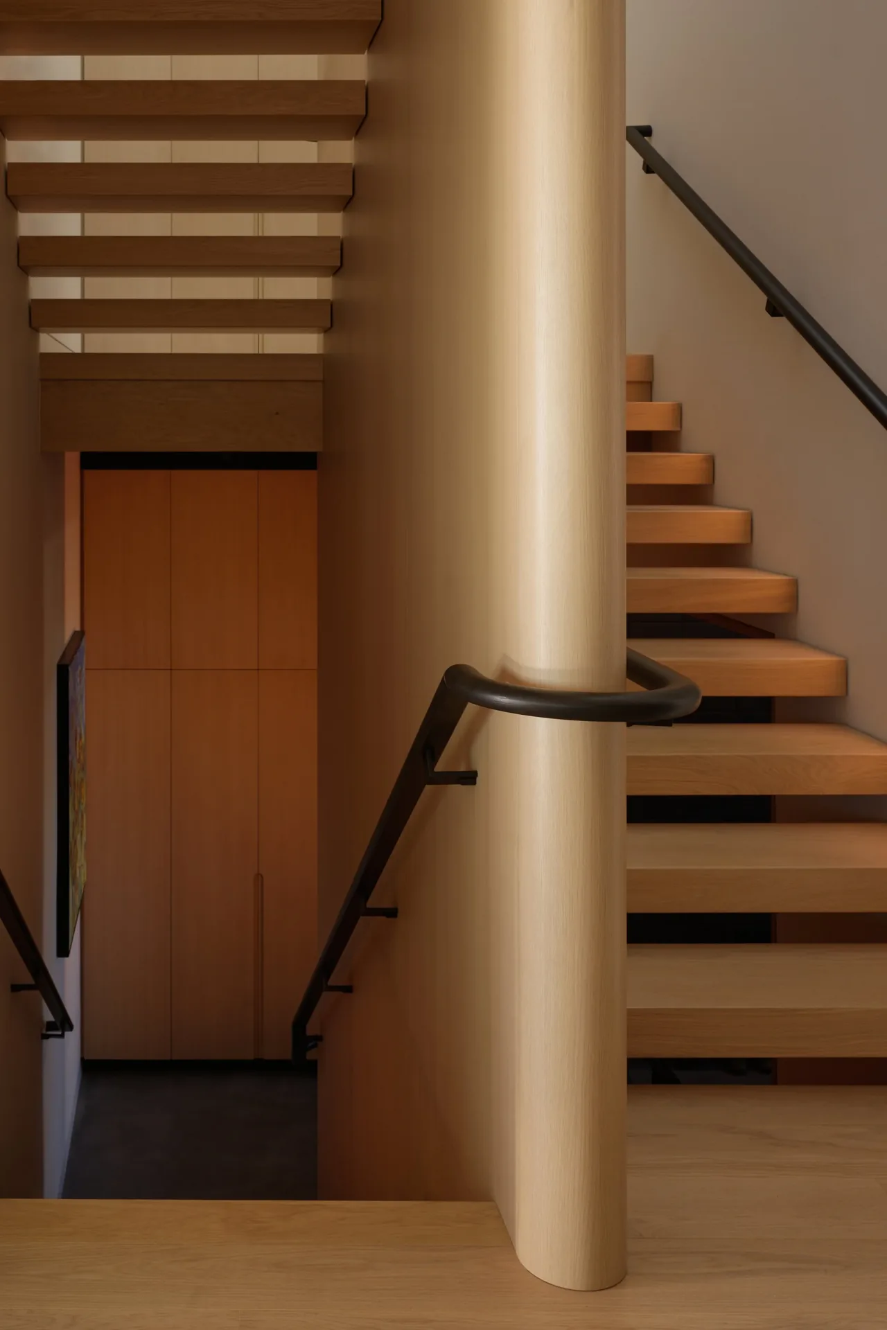 Floating wood stairs with black metal handrails and a rounded wood column at View Point Residence in Seattle.