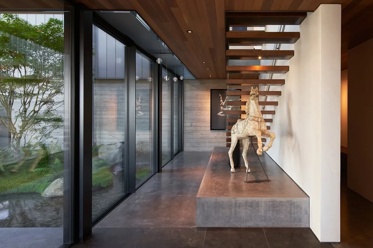 Hallway with floor-to-ceiling glazing, floating wood stairs, and a concrete display bench with horse sculpture.