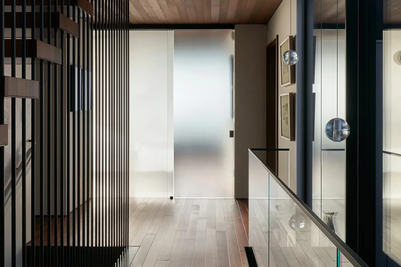 Hallway features vertical metal balusters, wood ceiling, hardwood floor, and a frosted glass sliding door.