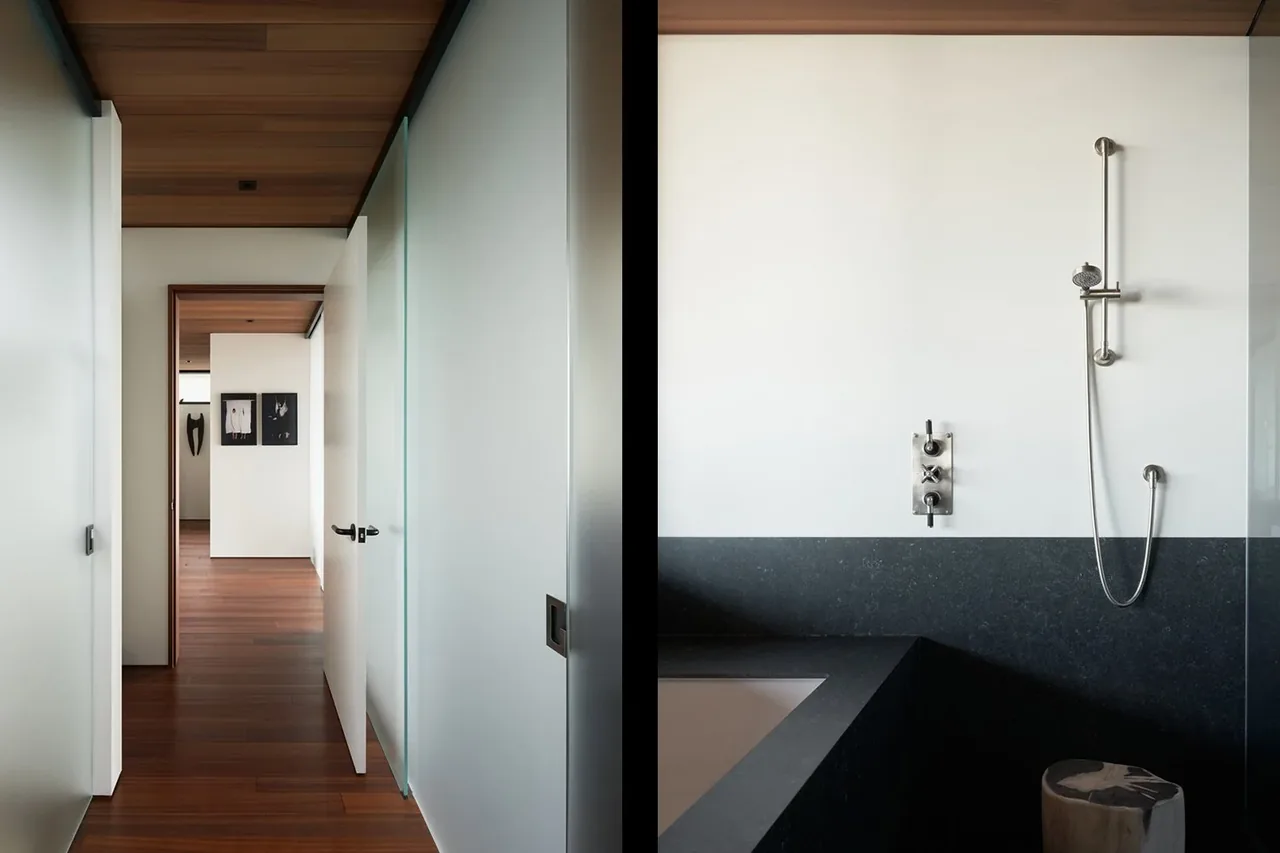 Hallway with wood plank flooring and ceiling opening to a bathroom featuring a dark stone bathtub and a handheld shower.