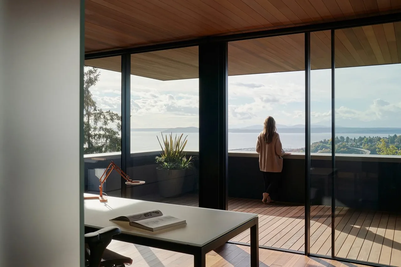 Office space opens to a balcony with wood plank decking and ceiling, overlooking a distant water and landscape view.