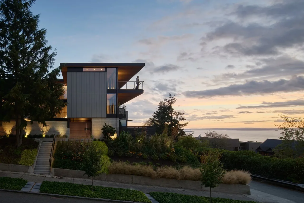 Modern home with cantilevered decks and large glass windows facing a water view at sunset.