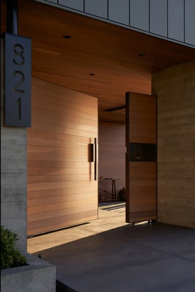 The Perch features a wide wood-paneled pivot front door framed by concrete walls and ceilings.