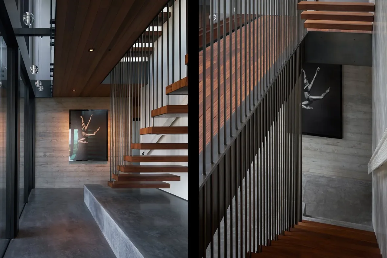 Modern floating wood stair with vertical metal balusters adjacent to concrete and wood-paneled walls.