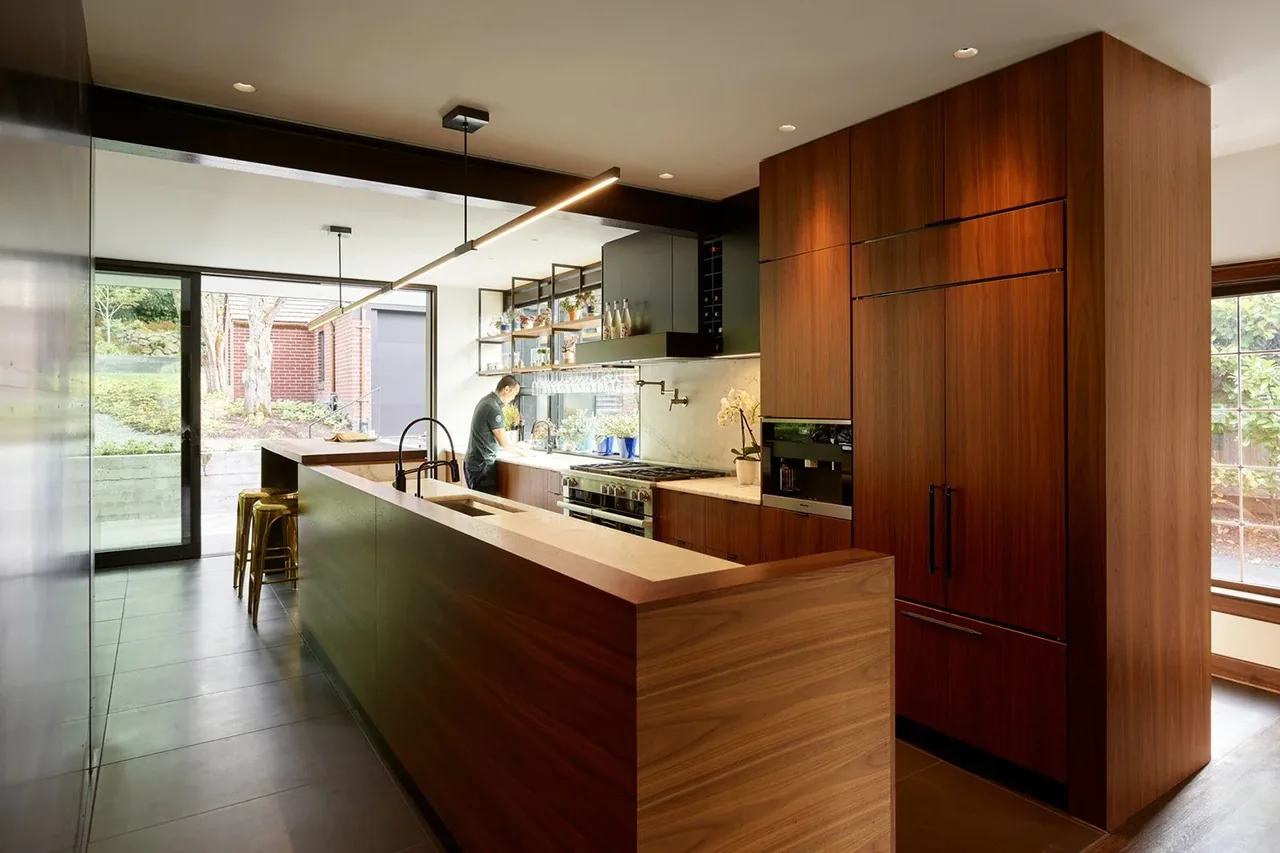 Kitchen in the past present house features wood cabinets, built-in appliance paneling, and floor-to-ceiling glass doors to the outside.