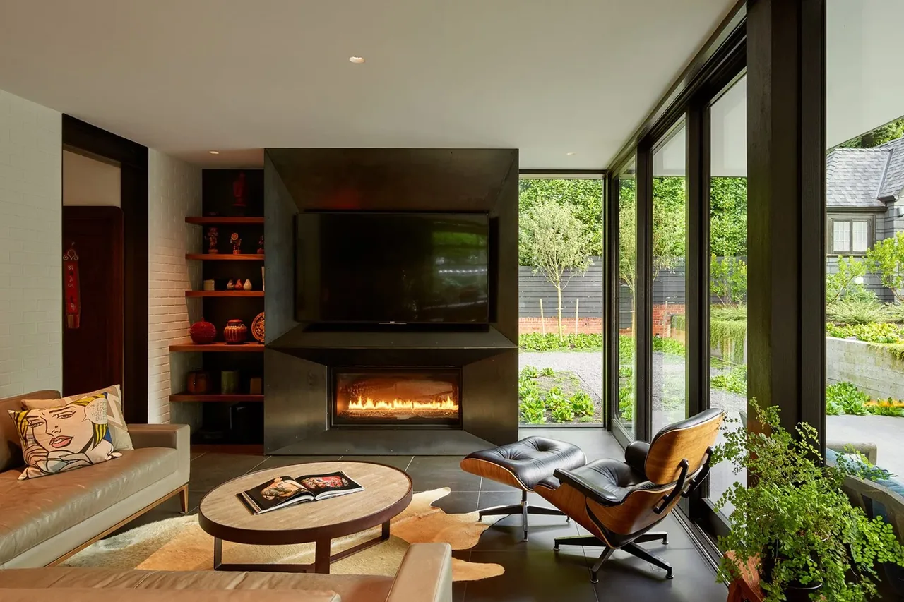Living room in the Past Present House features a black fireplace, floor-to-ceiling glazing, and leather seating with garden views.