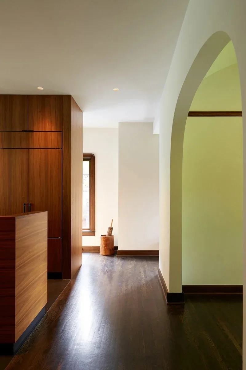 Hallway with dark hardwood floor, white walls, wooden built-in cabinetry, and an arched doorway.