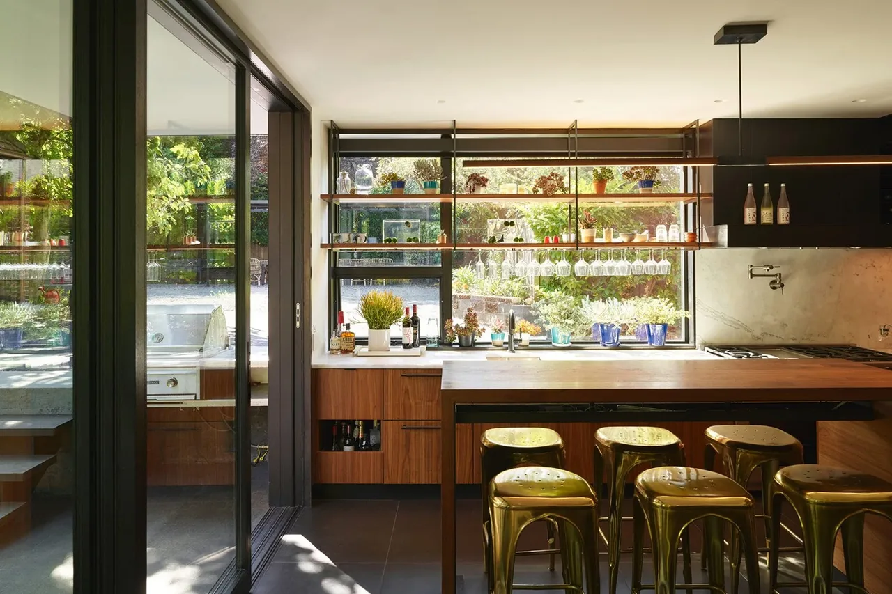 Kitchen interior featuring wooden cabinetry, open shelving with plants and glasses, and metallic gold stools at the island.