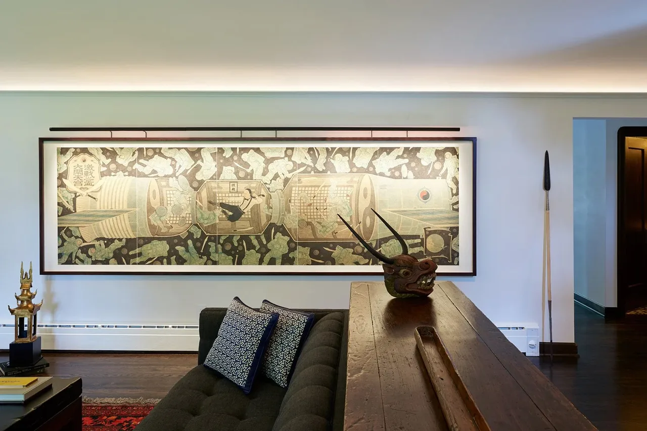 Living room with dark-stained wood floors, black tufted sofa with patterned pillows, and a long framed artwork on the wall.