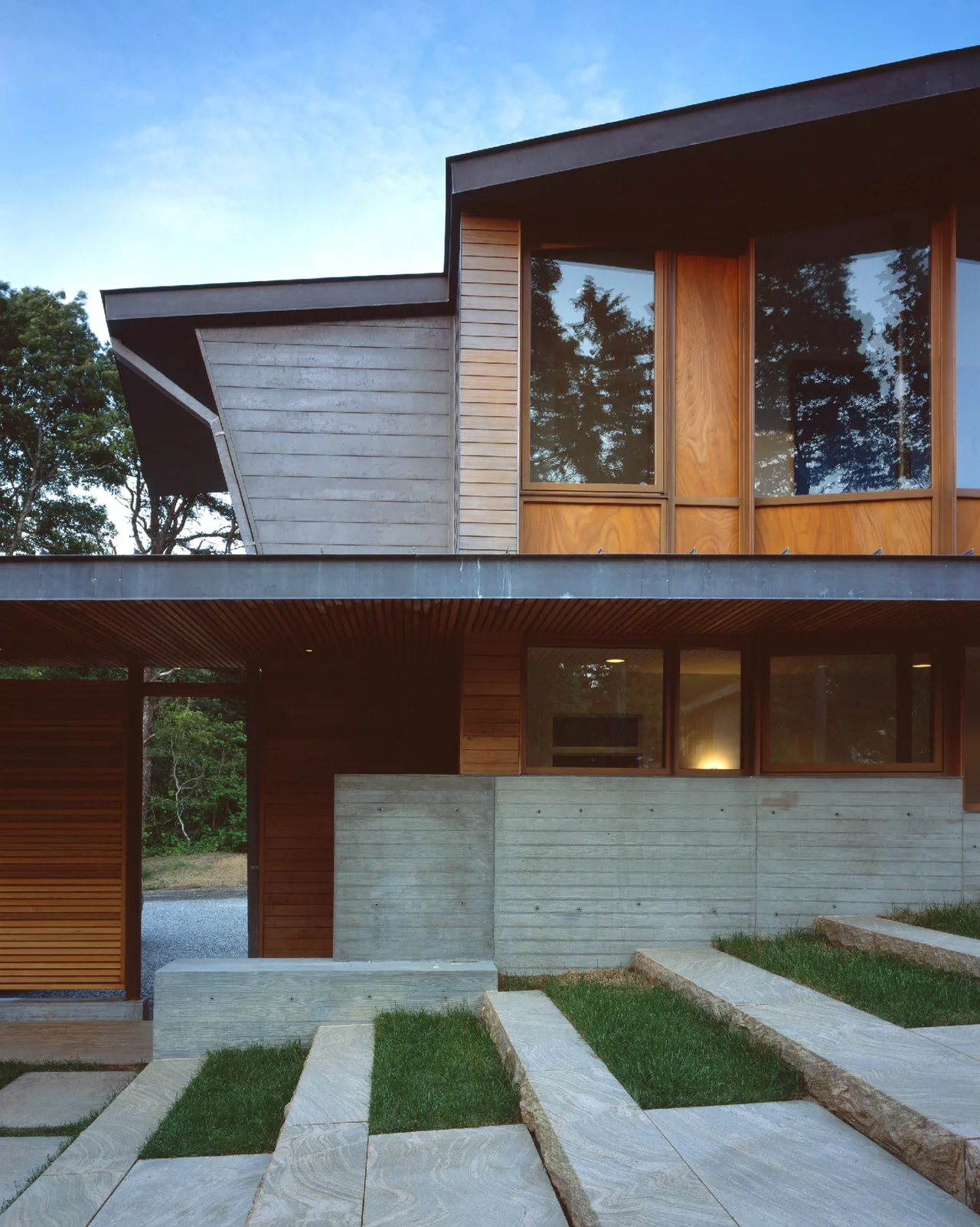 Orleans House in Cape Cod features wood siding, large windows, and concrete stairs integrated with landscaping.
