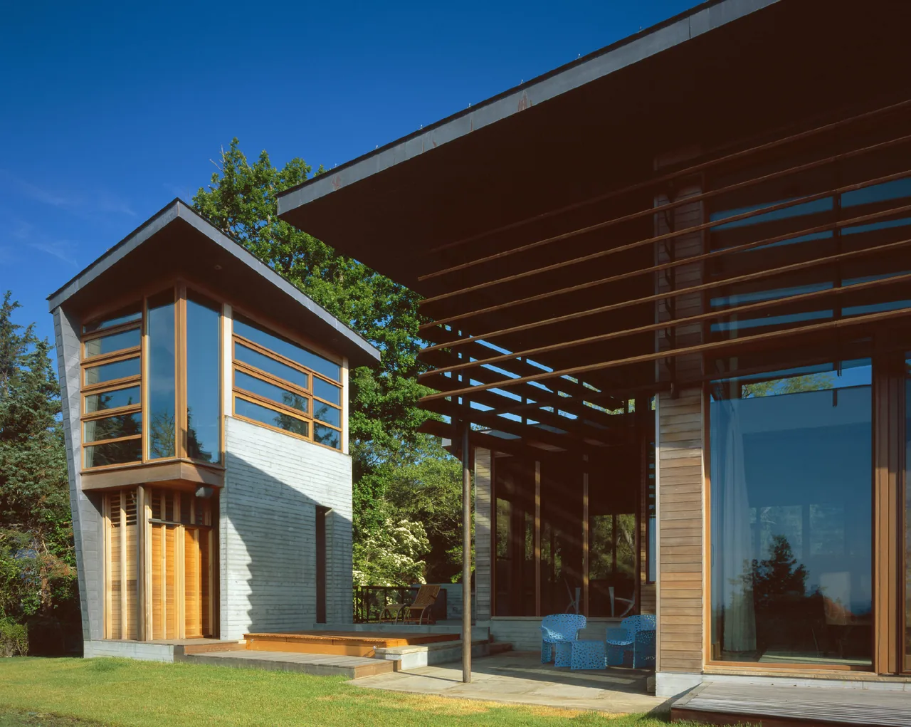 Orleans House features modern design with wood siding, large horizontal windows, and a pergola covered outdoor space.