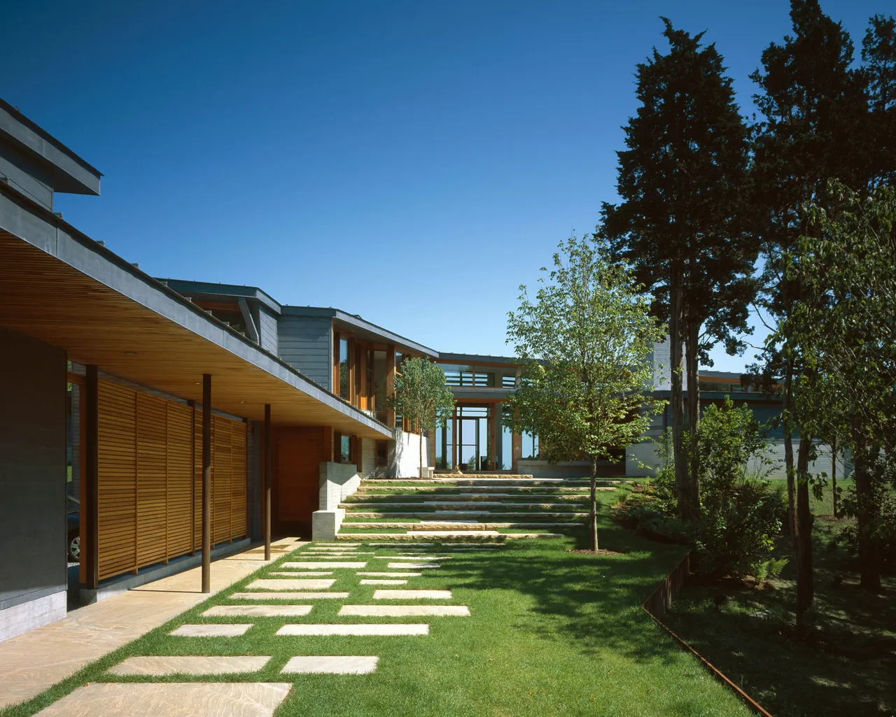 Orleans House features wood siding, horizontal wooden slats, and a patterned stone pathway leading to concrete stairs.