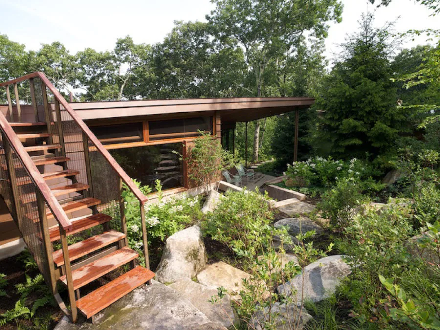 Chilmark Guest House features wood paneling, an exterior stair, and landscaped rock garden with forest surroundings.