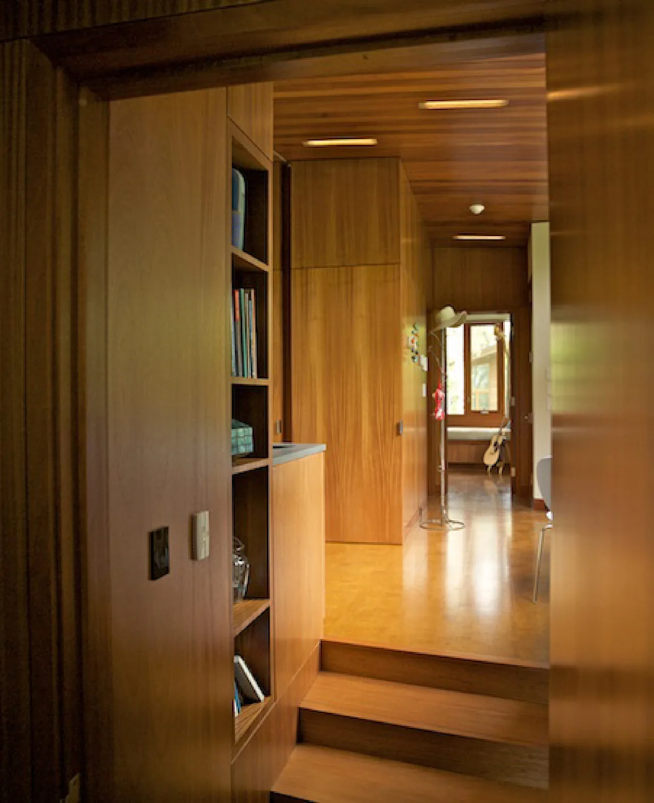Interior hallway in the Chilmark Guest House features wood paneling and built-in shelving, with a view to a room at the end with a guitar.