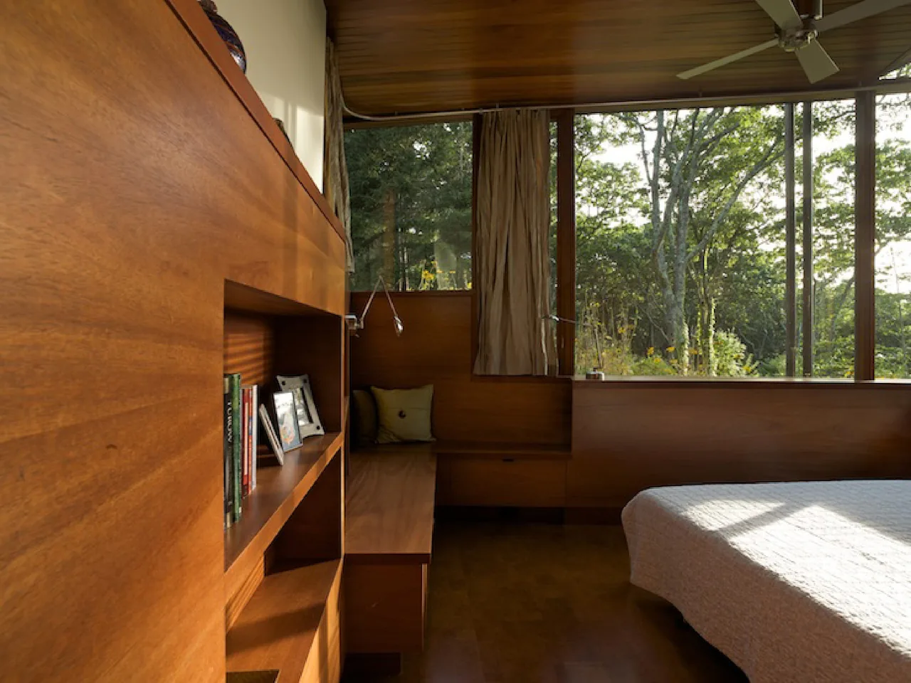 Wood-paneled bedroom with built-in seating and large windows showcasing forest views.
