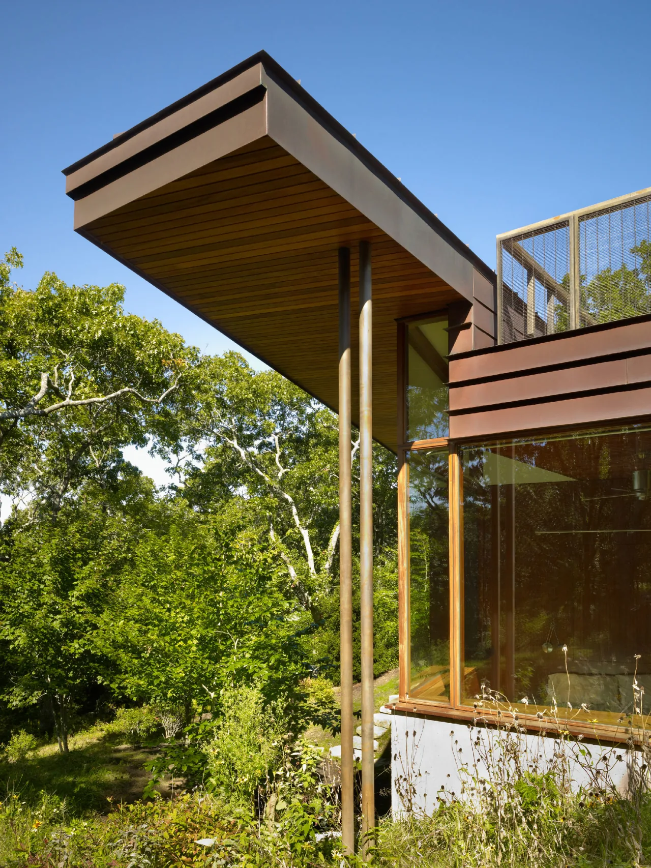 The Chilmark Guest House features a cantilevered roof supported by metal posts, with large glass windows and wood paneling.