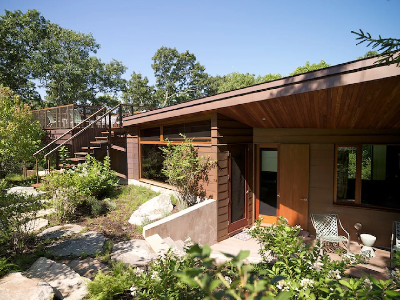 Chilmark Guest House exterior in Massachusetts features wood siding, wood soffit ceiling, metal posts, and large glass panels.