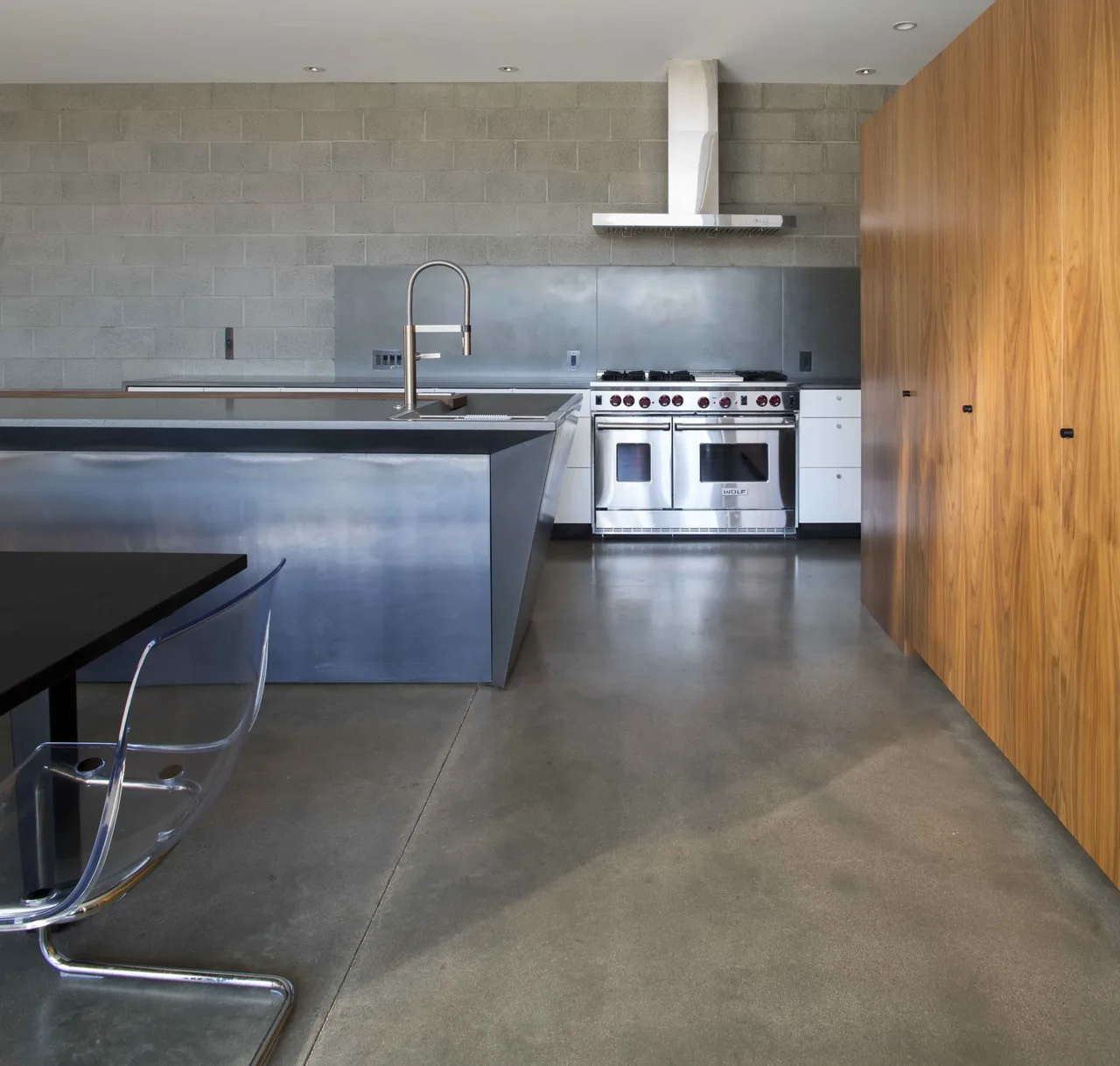 Kitchen in the Staab residence featuring a stainless steel island, concrete block backsplash, and wood-paneled cabinetry.