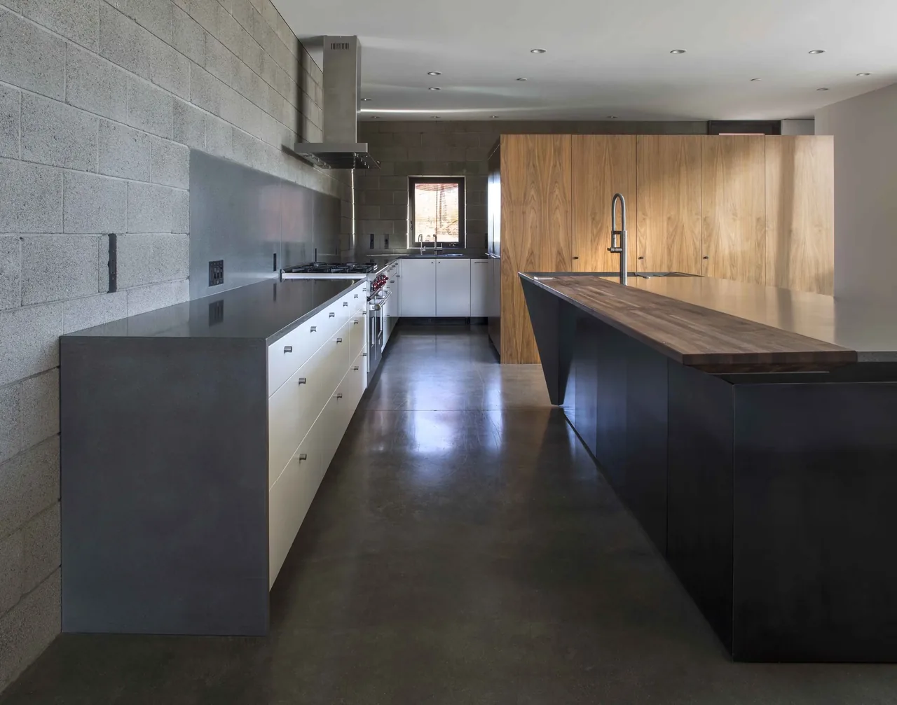 Staab residence kitchen features polished concrete flooring, concrete block walls, and a dual-tone island with wood and metal finishes.