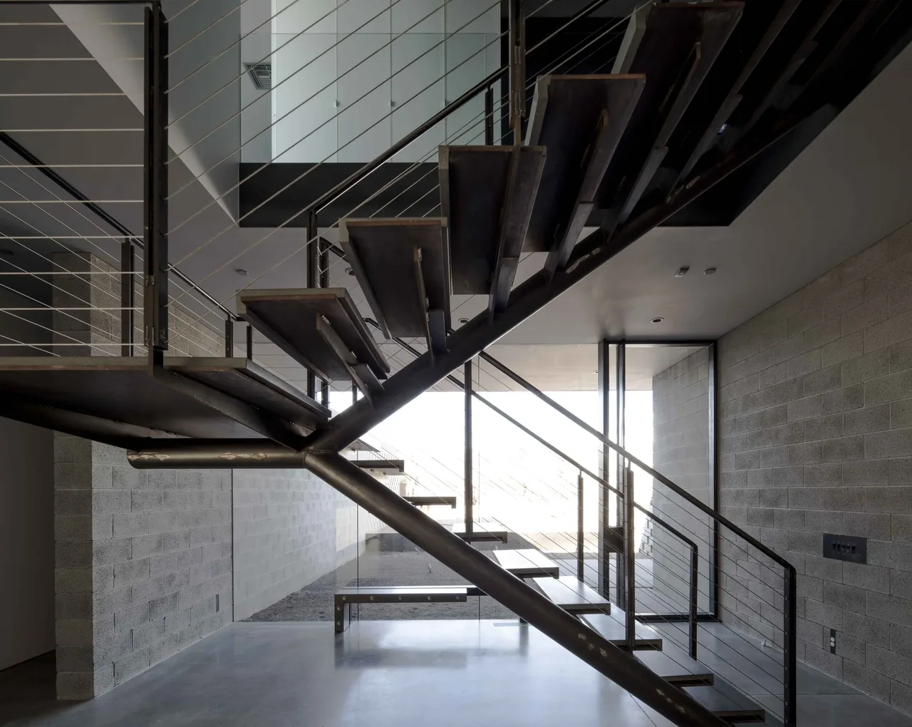 Modern floating metal staircase with cable railing in a concrete block interior space of the Staab residence.