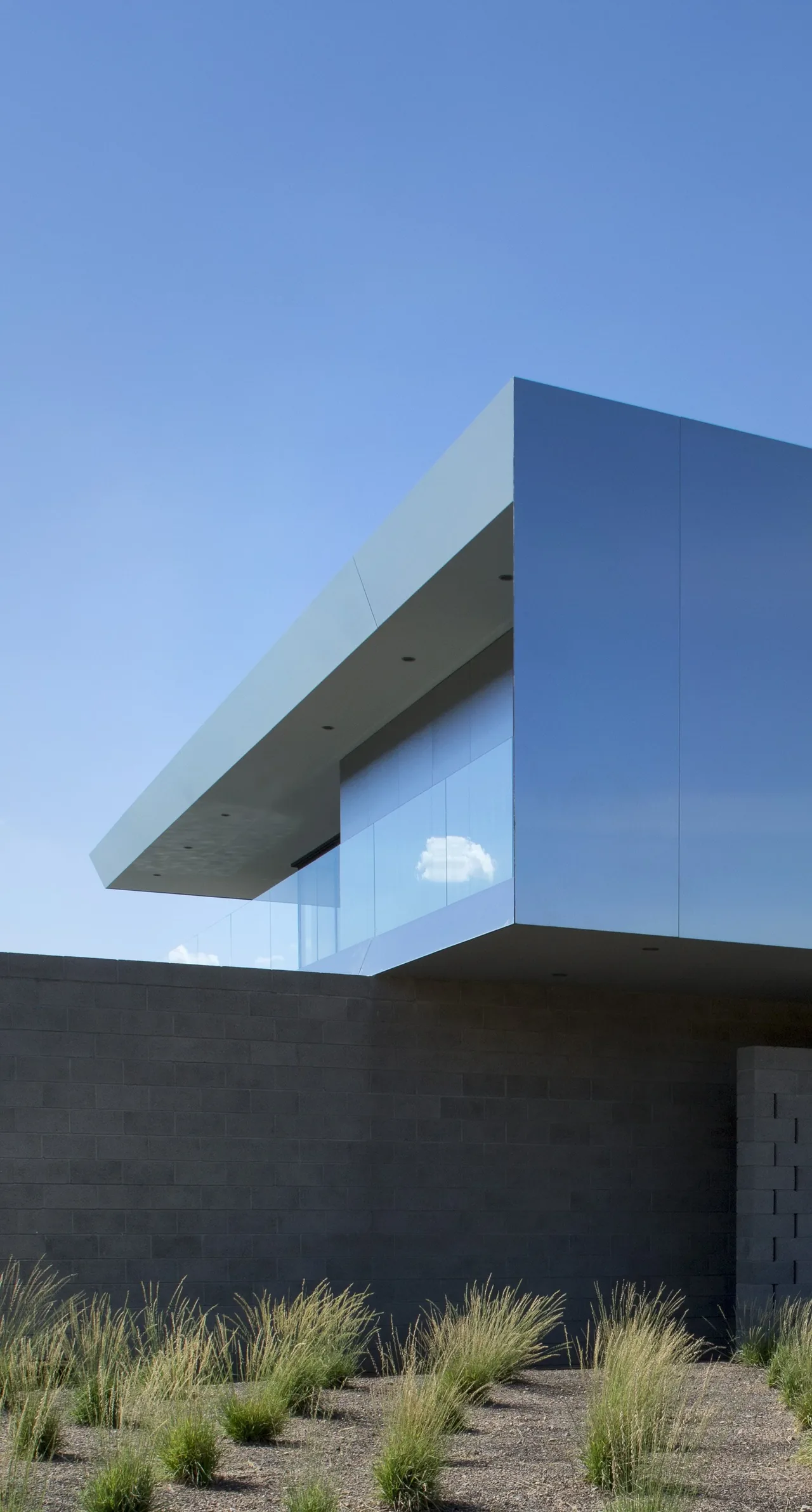 The Staab Residence features a cantilevered reflective metal volume above a concrete block wall with desert plants below.