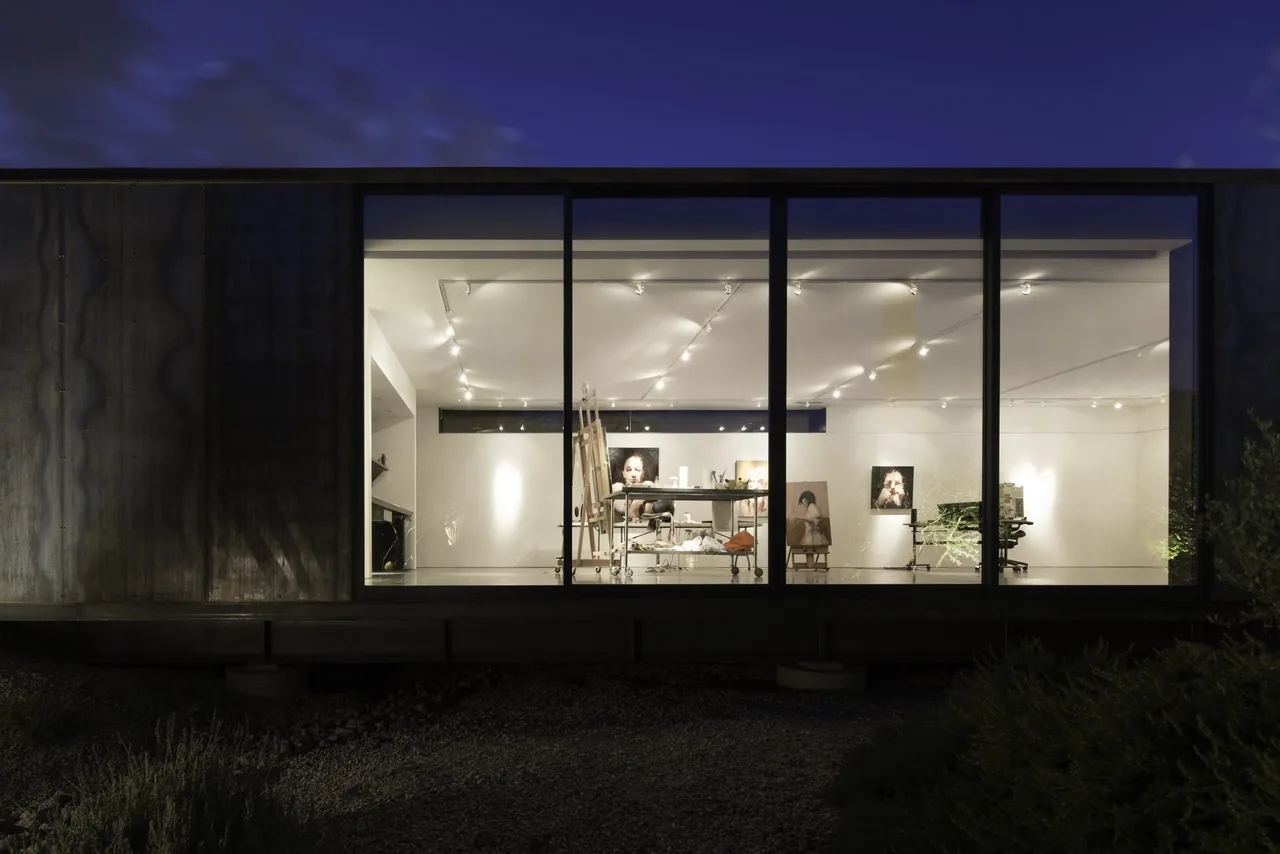Interior of a modern art studio illuminated at night with large floor-to-ceiling glazing and track lighting.