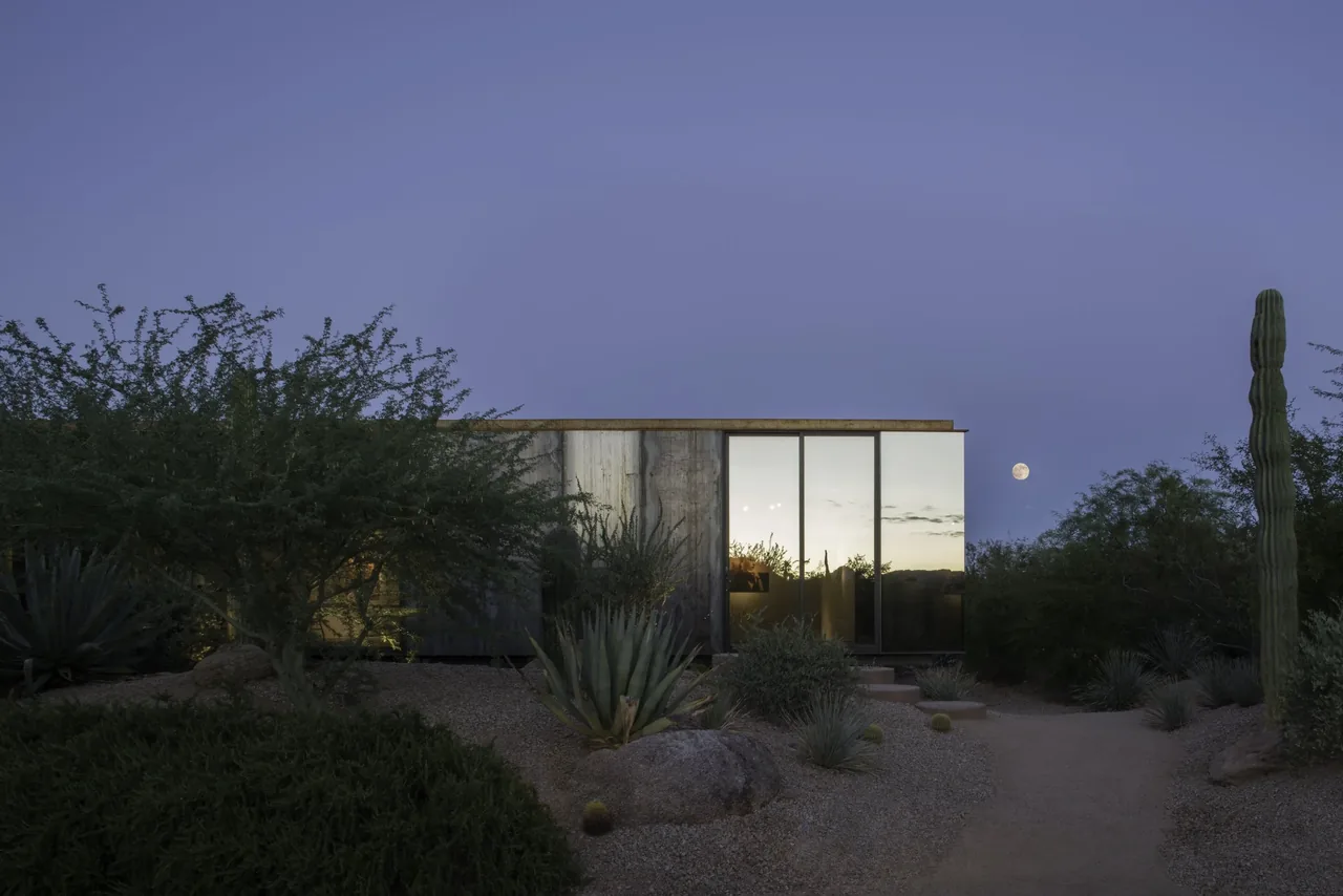 Project six by Chen Suchart Studio shows a desert home with concrete walls, large glass windows, and desert landscaping under a moonlit sky.