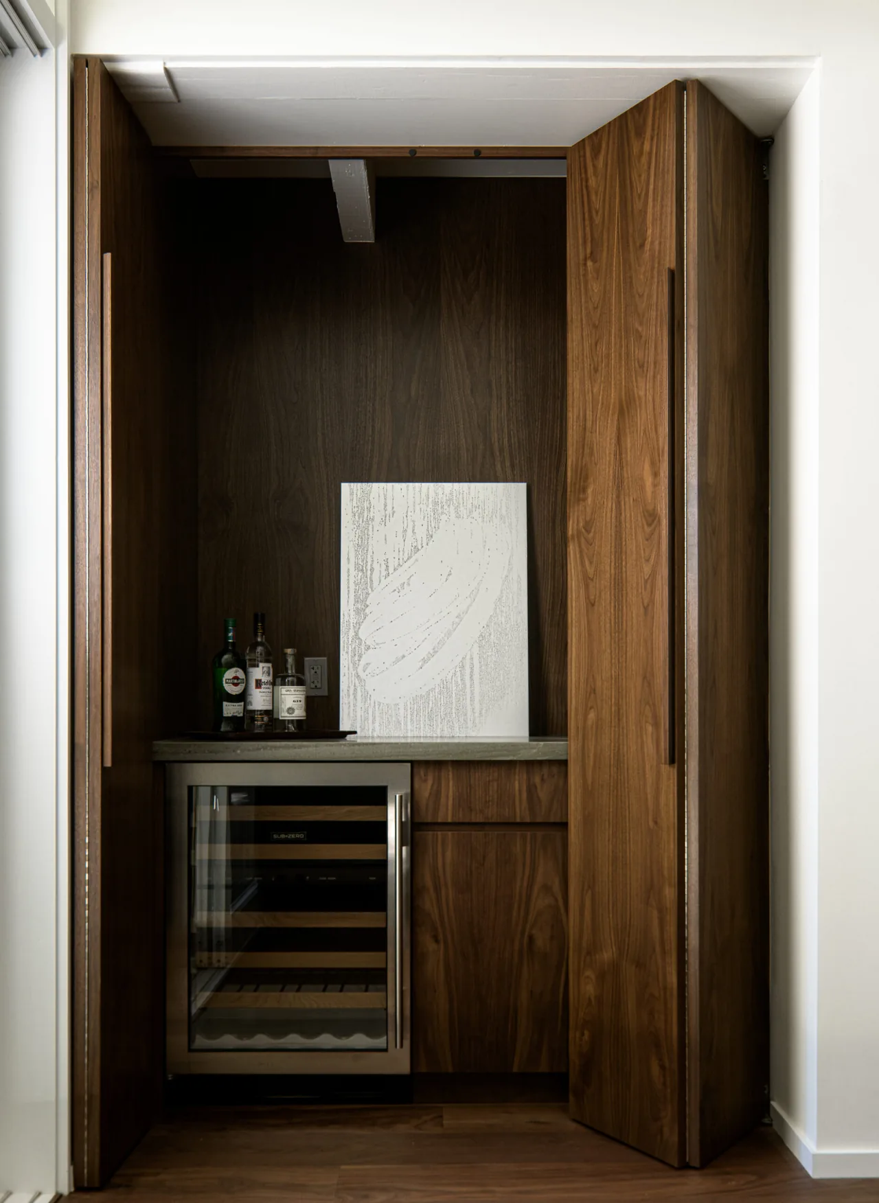 Wet bar with walnut cabinetry, concrete countertop, and a built-in wine fridge at Veneklasen House by CHU+GOODING Architects.