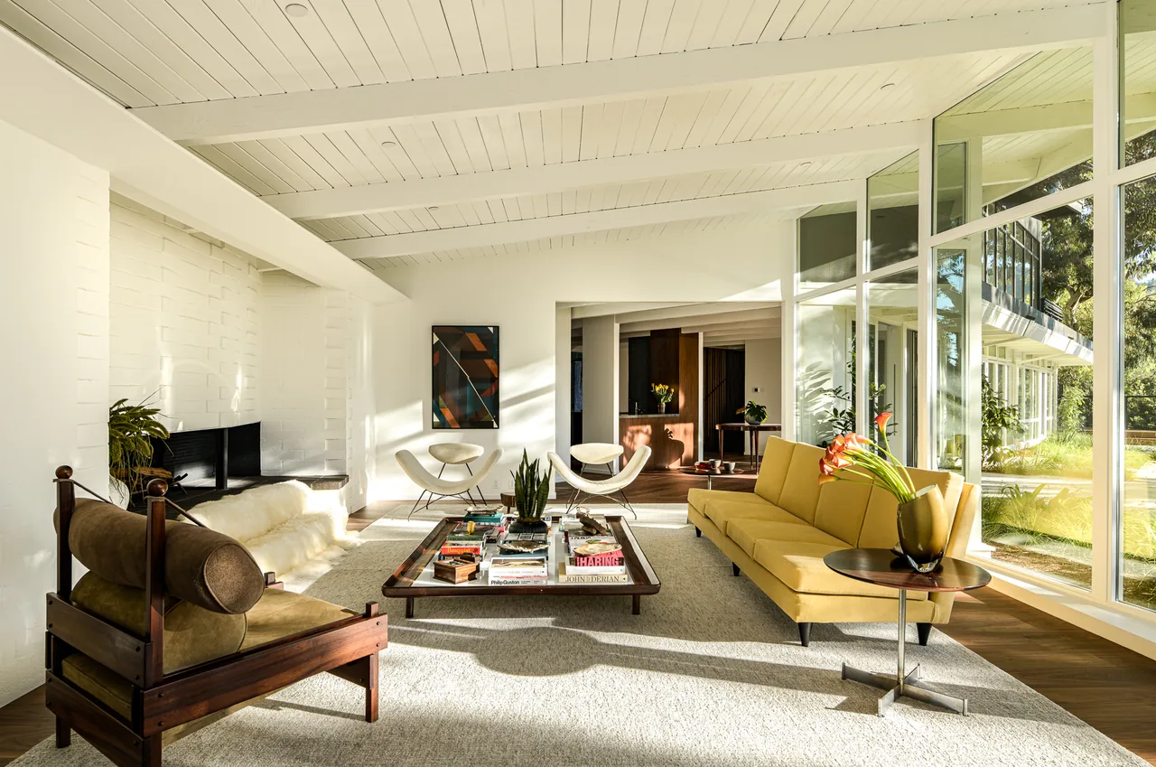 Living room with floor-to-ceiling glazing, exposed white ceiling beams, and midcentury furniture in the Veneklasen House.