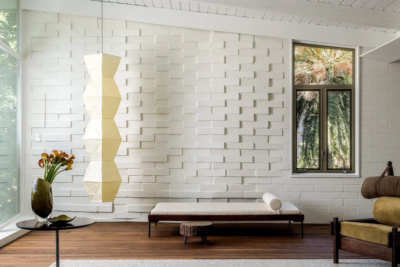 Living area features a white textured brick wall, wood flooring, large window, and minimalist furniture.