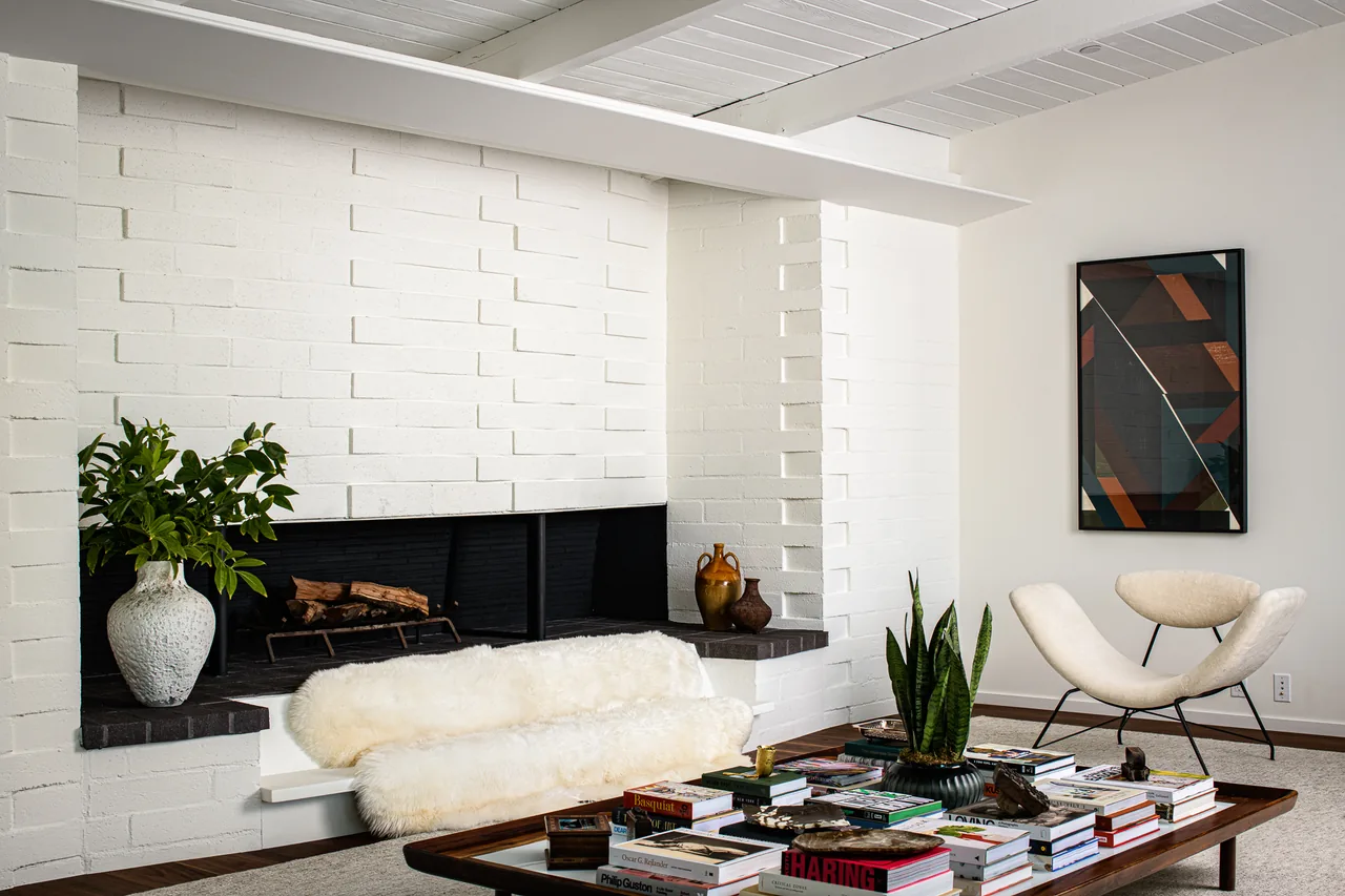 Living room of the Veneklasen House featuring a white brick fireplace, a curved white lounge chair, and a wood coffee table with books.