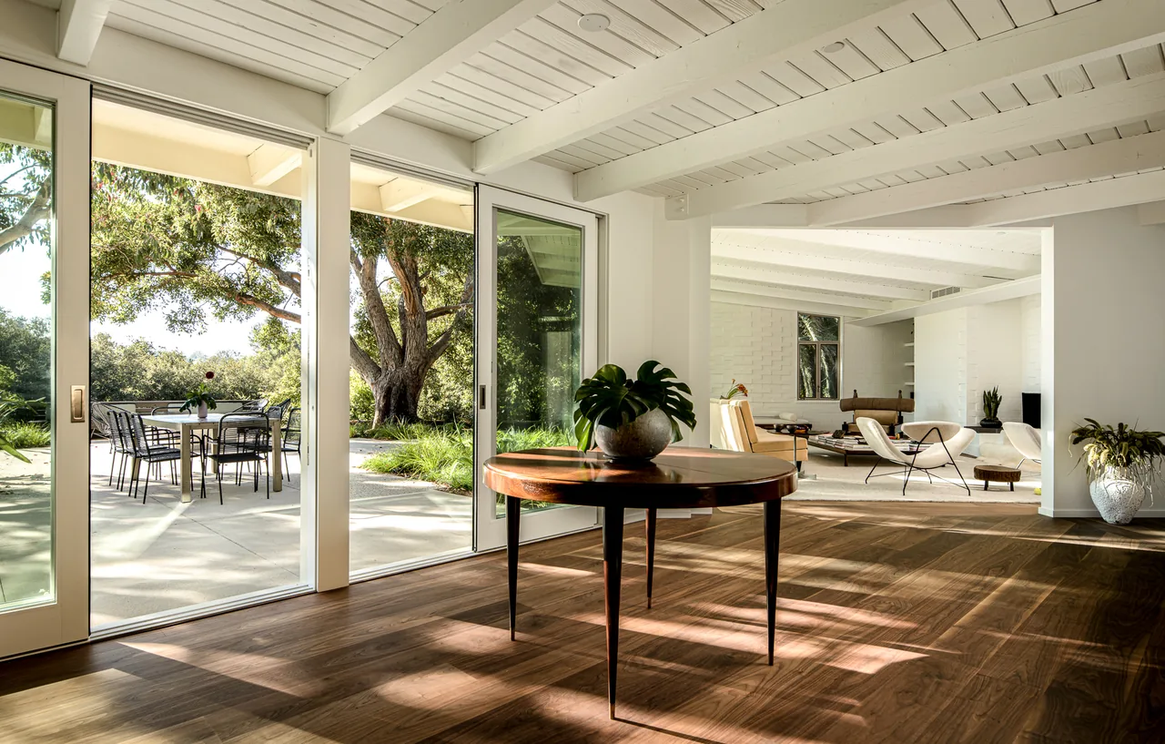 Veneklasen House living space with floor-to-ceiling glass doors offering access to an outdoor dining patio and views of landscaped yard.