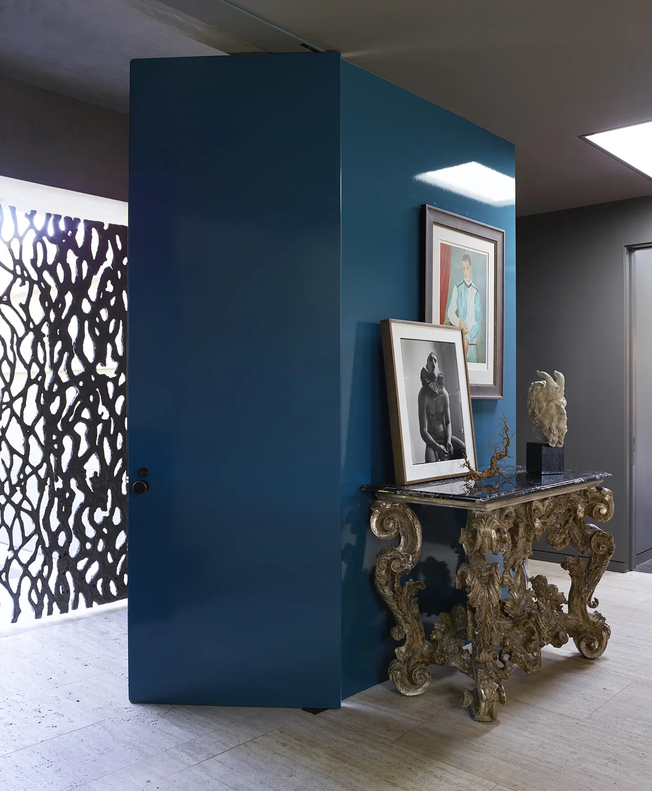 The Hollywood Hills House entry features a sculptural metal door and a richly detailed console table beneath framed artworks.
