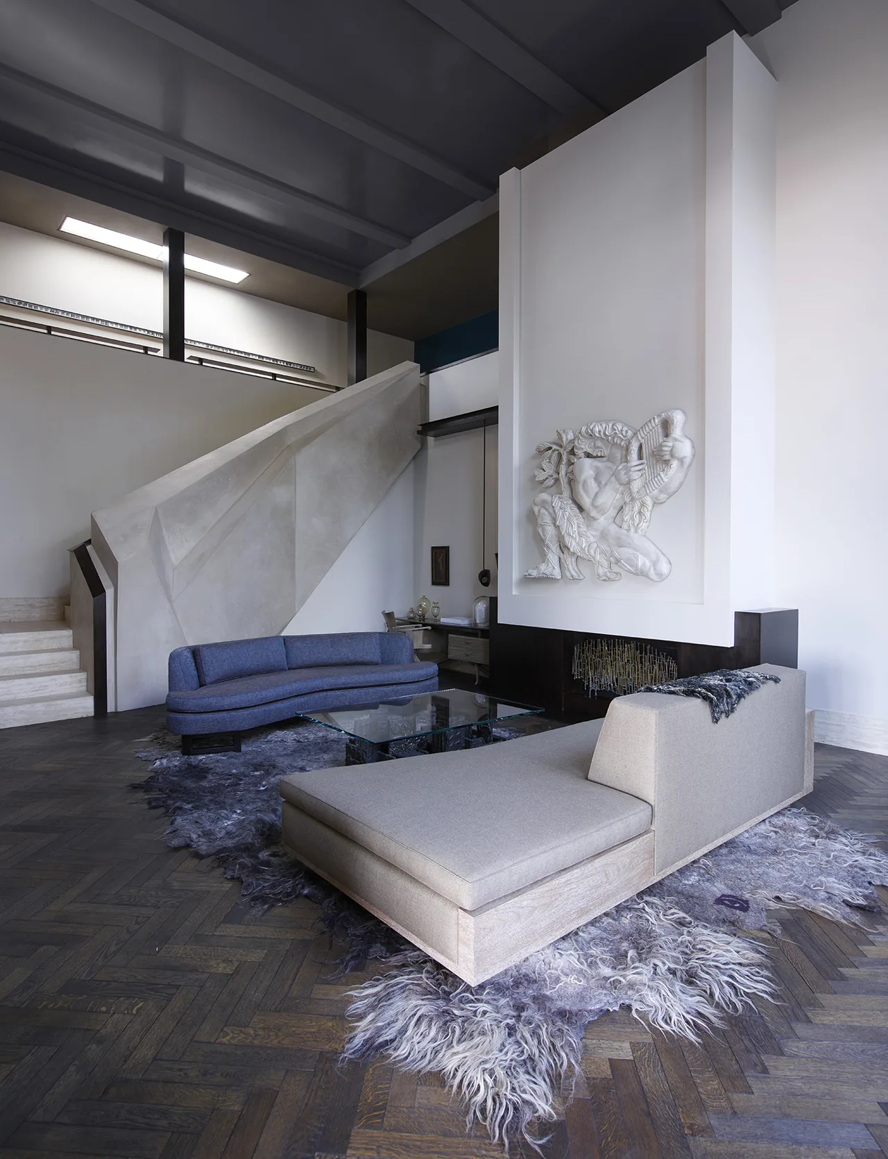 Open living room with a gray chaise lounge, a curved blue sofa, and a sculptural fireplace wall detail.